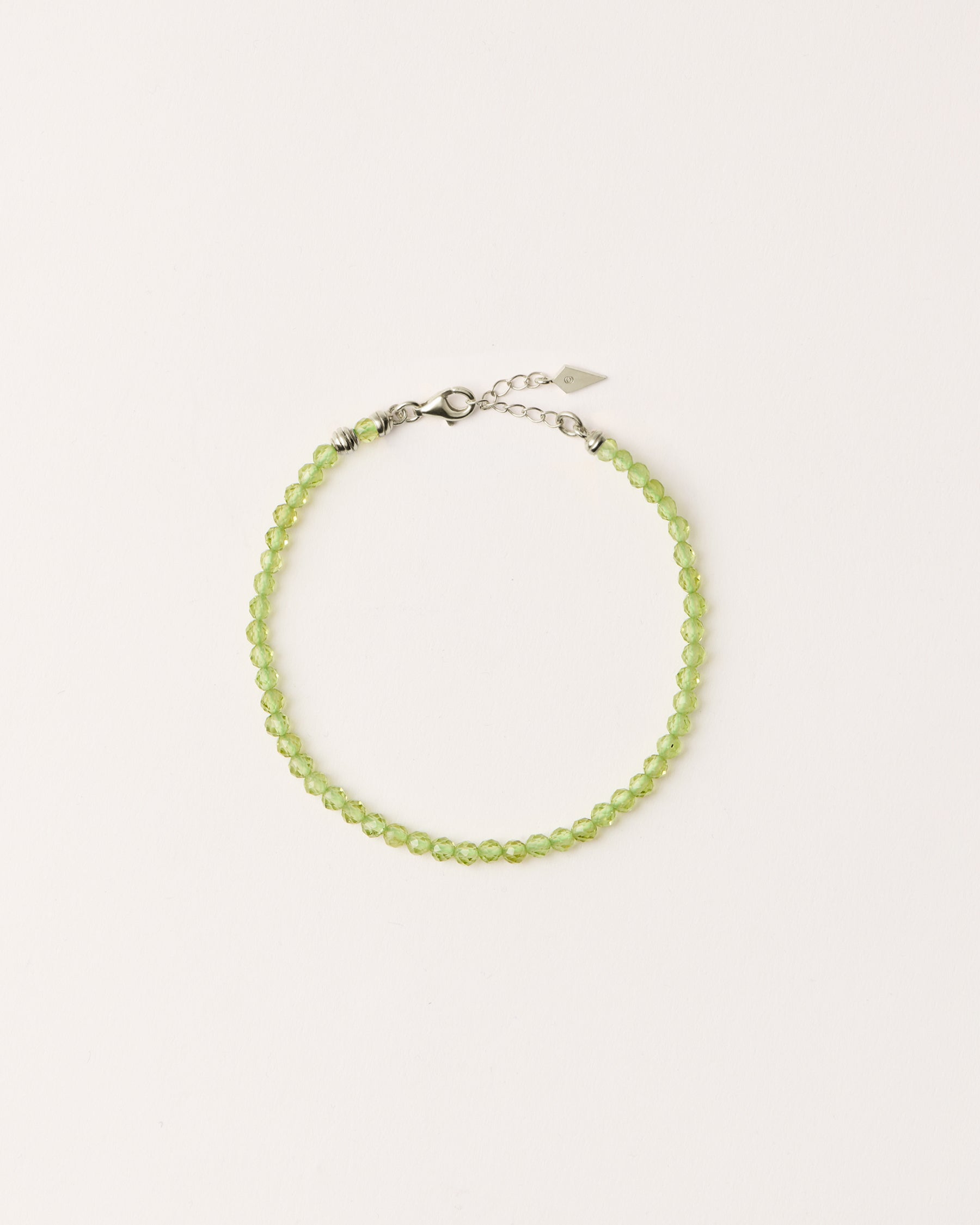 ETERNA OLMAR Peridot bracelet with polished silver spiral bead, 4 cm extension chain and clasp, arrowhead-shaped fantasy signature, and 4 mm faceted chrysolite bead strand.