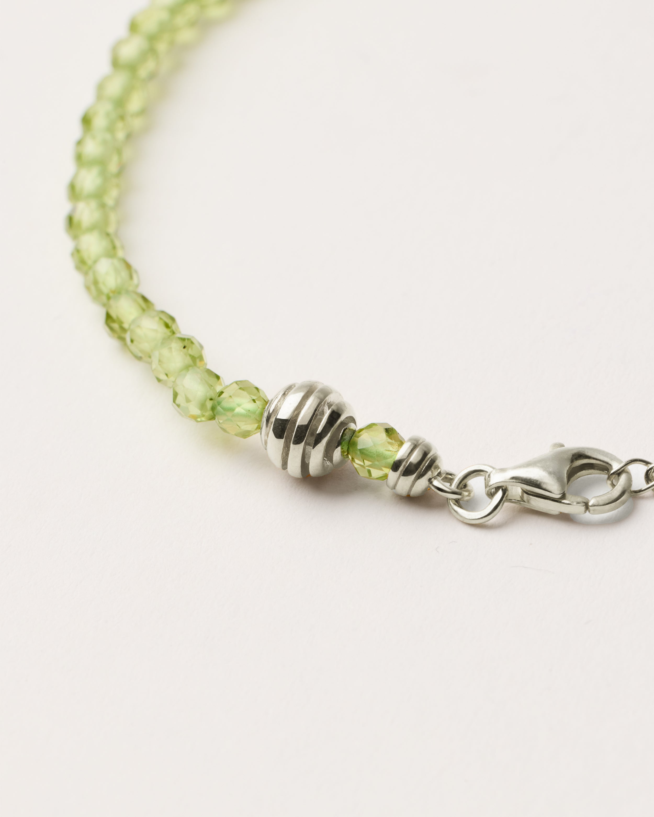 ETERNA OLMAR Peridot bracelet with polished silver spiral bead, 4 cm extension chain and clasp, arrowhead-shaped fantasy signature, and 4 mm faceted chrysolite bead strand.