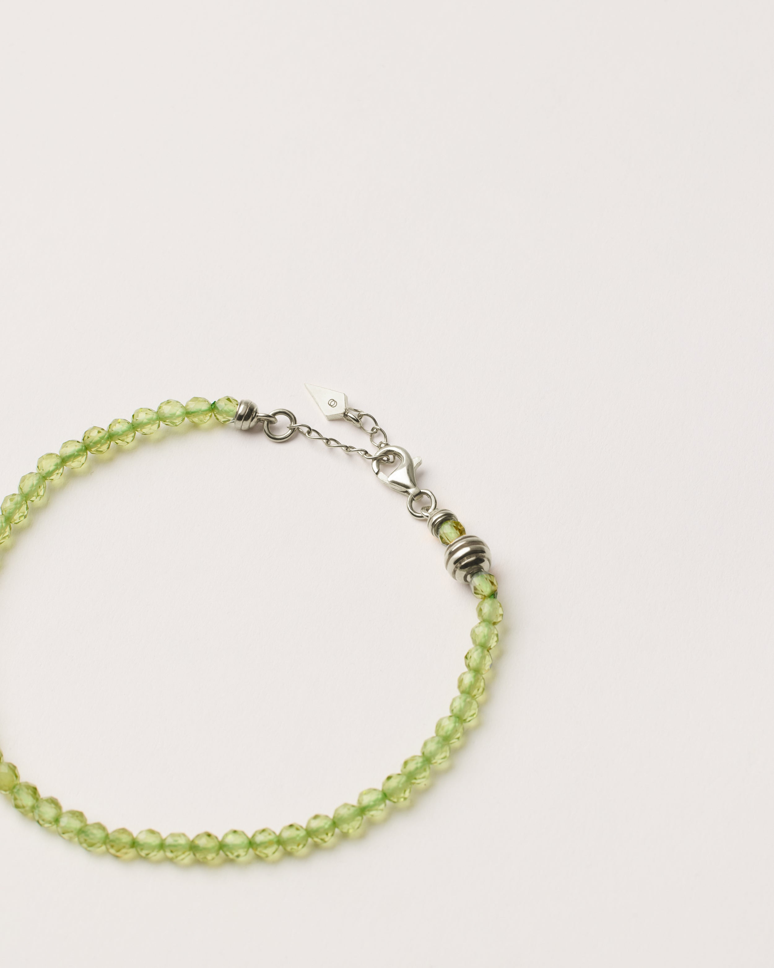 ETERNA OLMAR Peridot bracelet with polished silver spiral bead, 4 cm extension chain and clasp, arrowhead-shaped fantasy signature, and 4 mm faceted chrysolite bead strand.