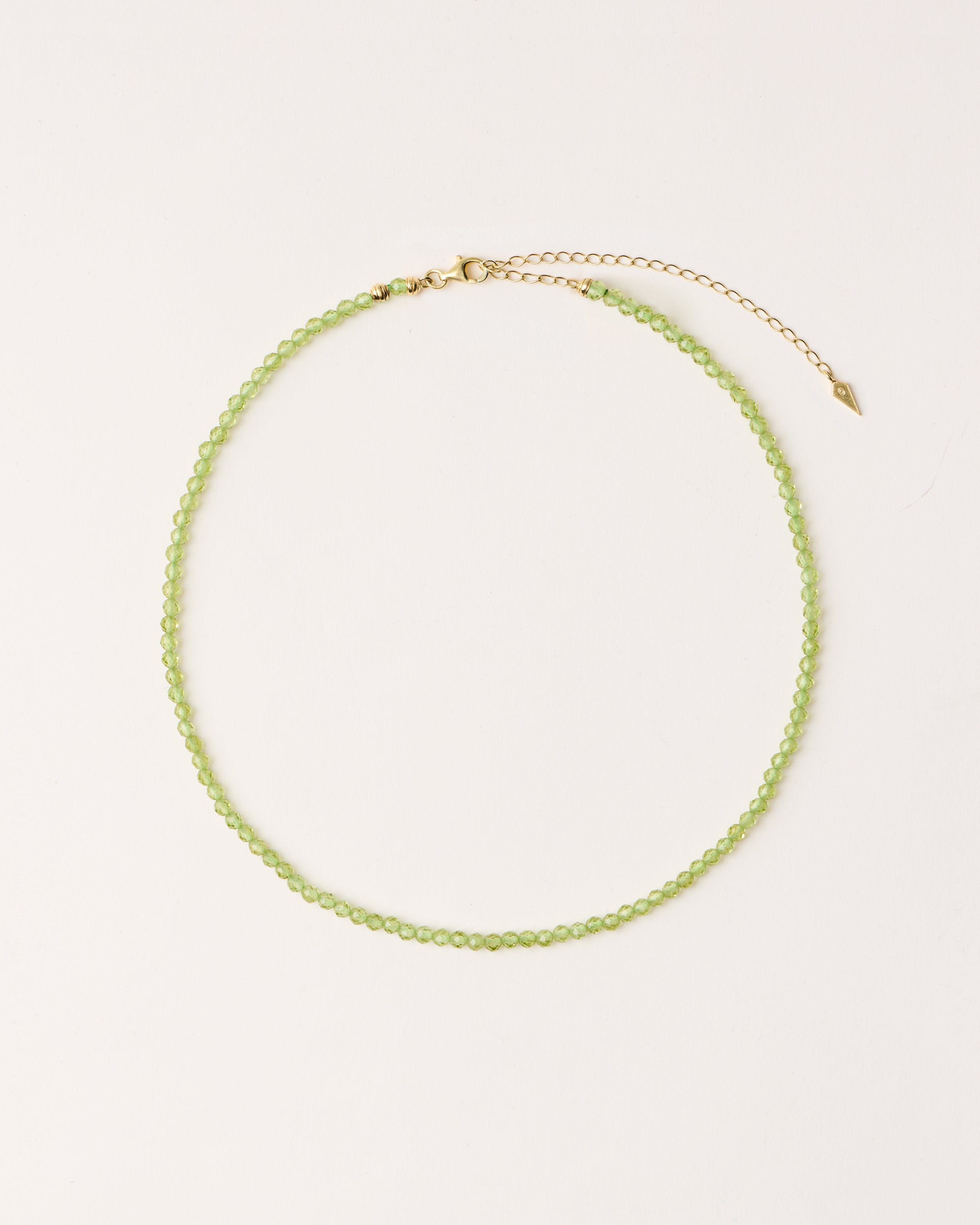 ETERNA OLMAR Peridot necklace with polished gold spiral bead, 8 cm extension chain and clasp, arrowhead-shaped fantasy signature, and 4 mm faceted chrysolite bead strand.