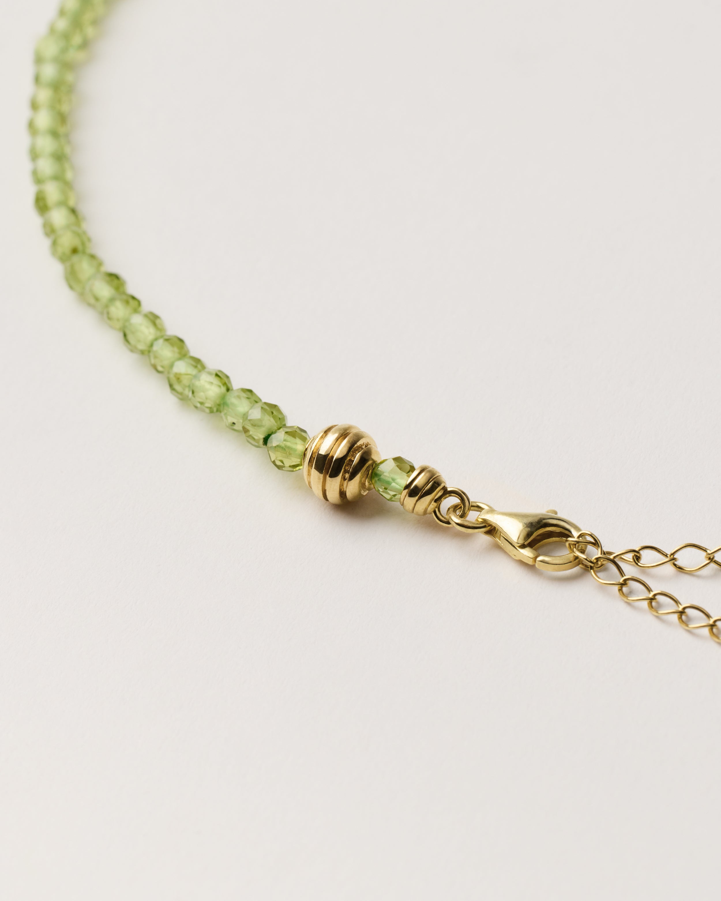 ETERNA OLMAR Peridot necklace with polished gold spiral bead, 8 cm extension chain and clasp, arrowhead-shaped fantasy signature, and 4 mm faceted chrysolite bead strand.