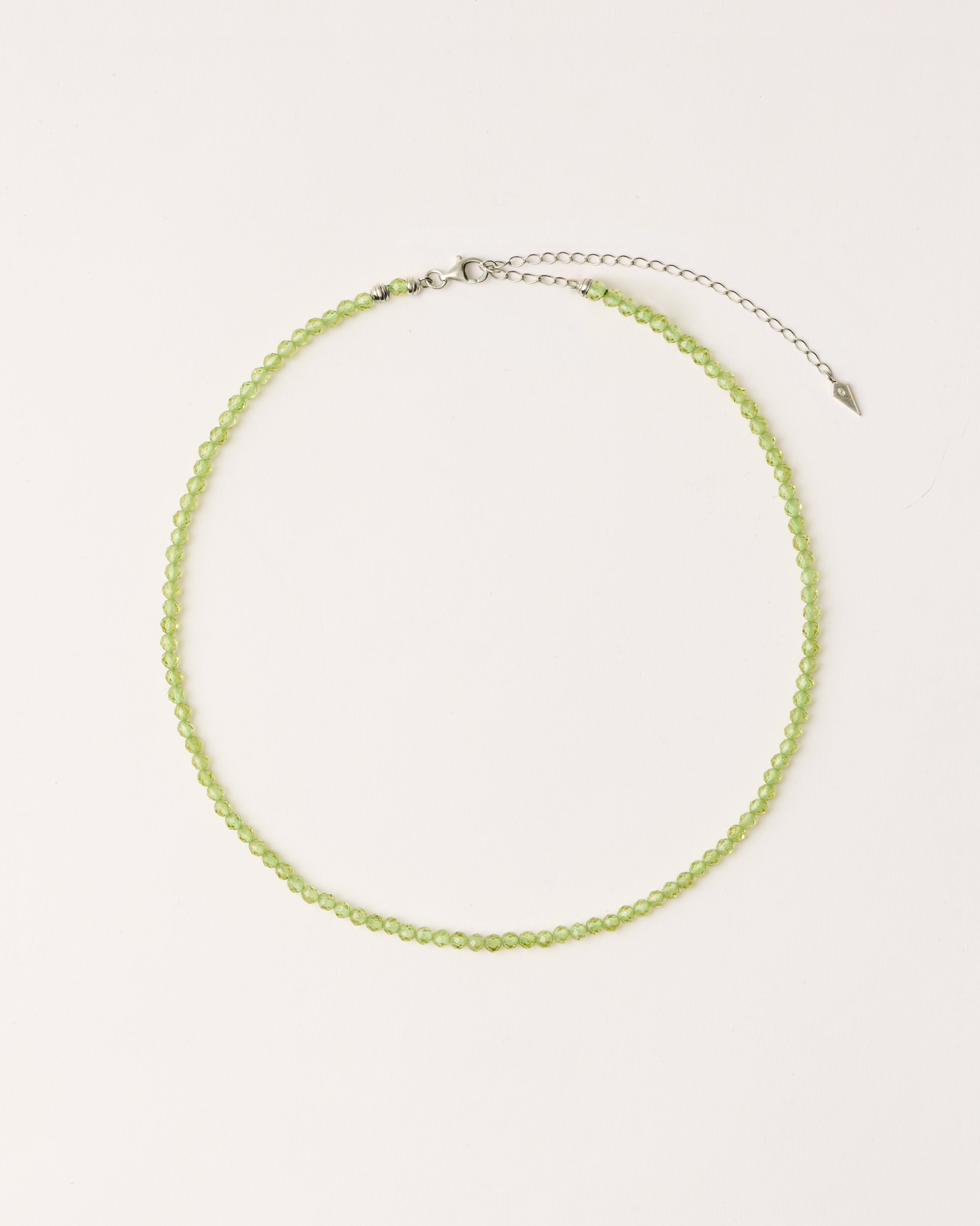 ETERNA OLMAR Peridot necklace with polished silver spiral bead, 8 cm extension chain and clasp, arrowhead-shaped fantasy signature, and 4 mm faceted chrysolite bead strand.