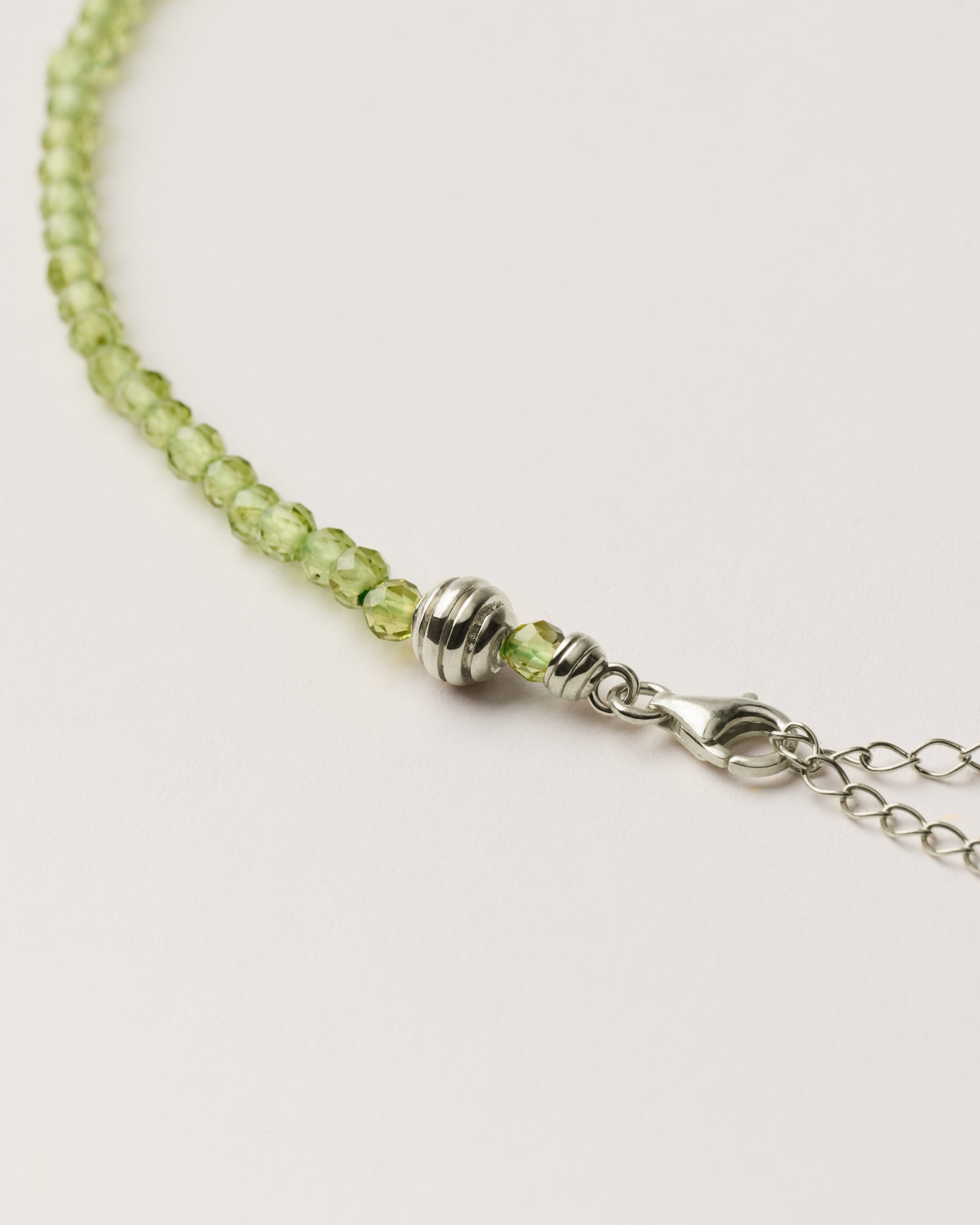 ETERNA OLMAR Peridot necklace with polished silver spiral bead, 8 cm extension chain and clasp, arrowhead-shaped fantasy signature, and 4 mm faceted chrysolite bead strand.