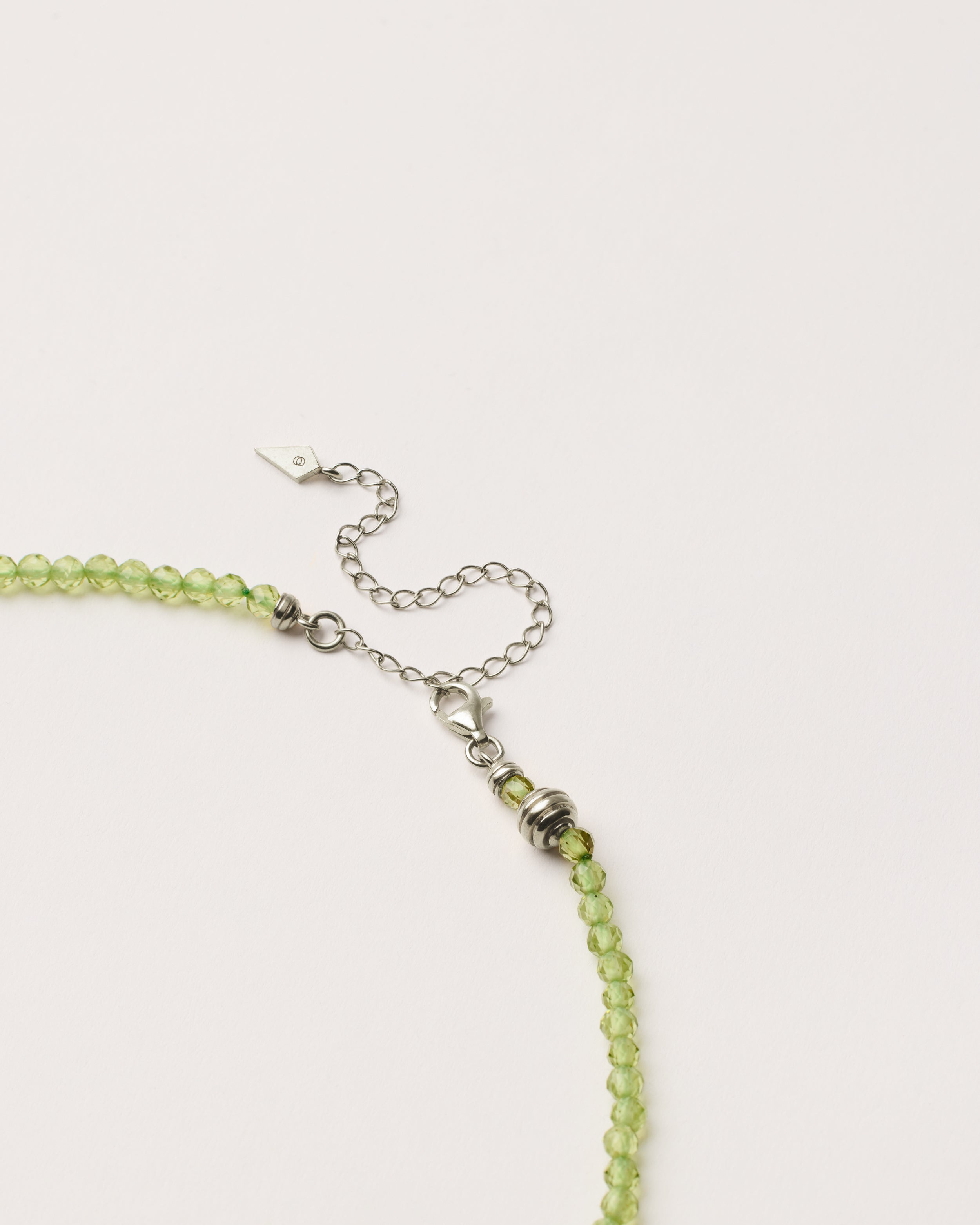 ETERNA OLMAR Peridot necklace with polished silver spiral bead, 8 cm extension chain and clasp, arrowhead-shaped fantasy signature, and 4 mm faceted chrysolite bead strand.