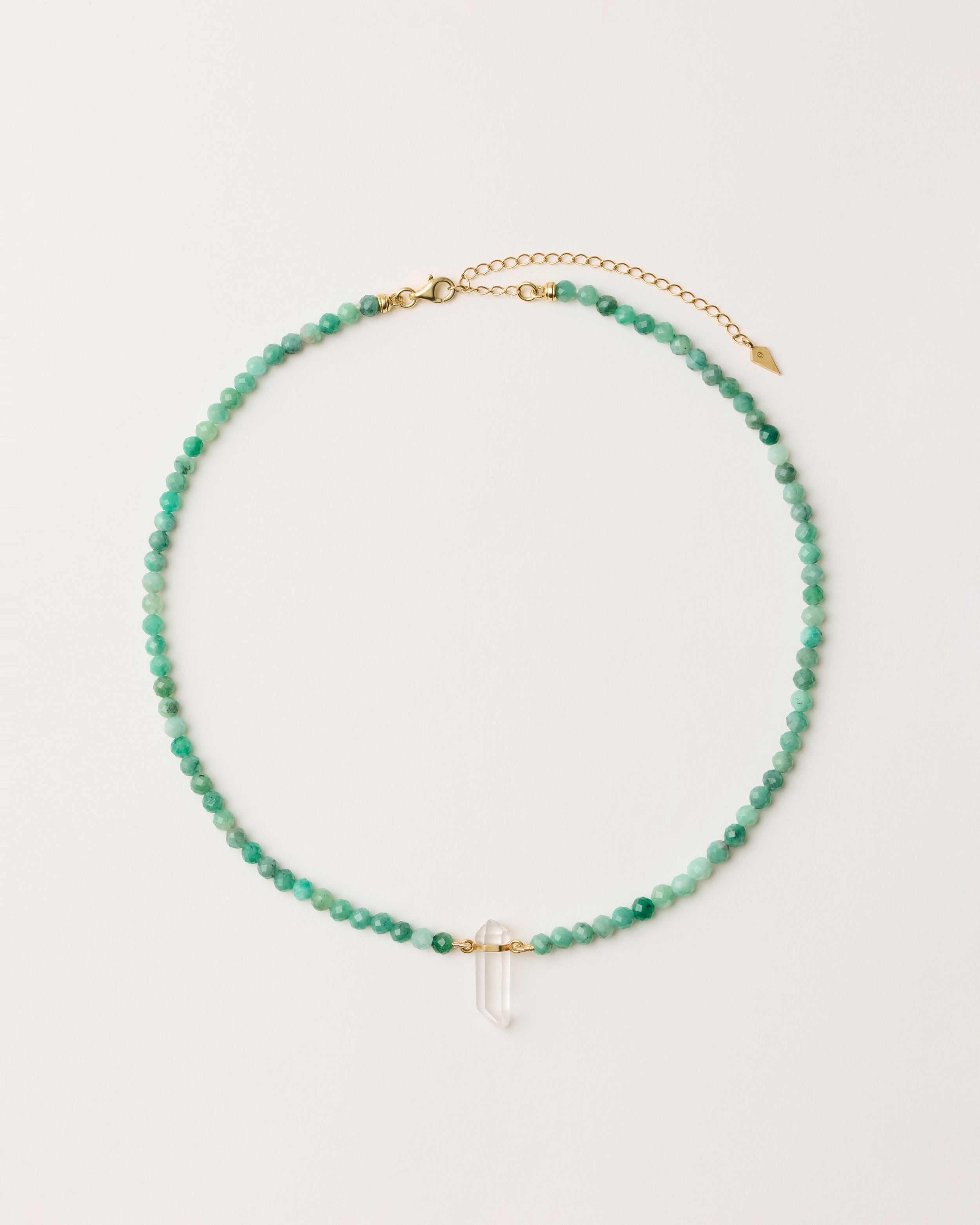 ENCARA VIRID Emerald necklace with raw polished quartz point pendant, gold 8 cm extension chain and clasp, arrowhead-shaped fantasy signature, and 4 mm faceted emerald bead strand.
