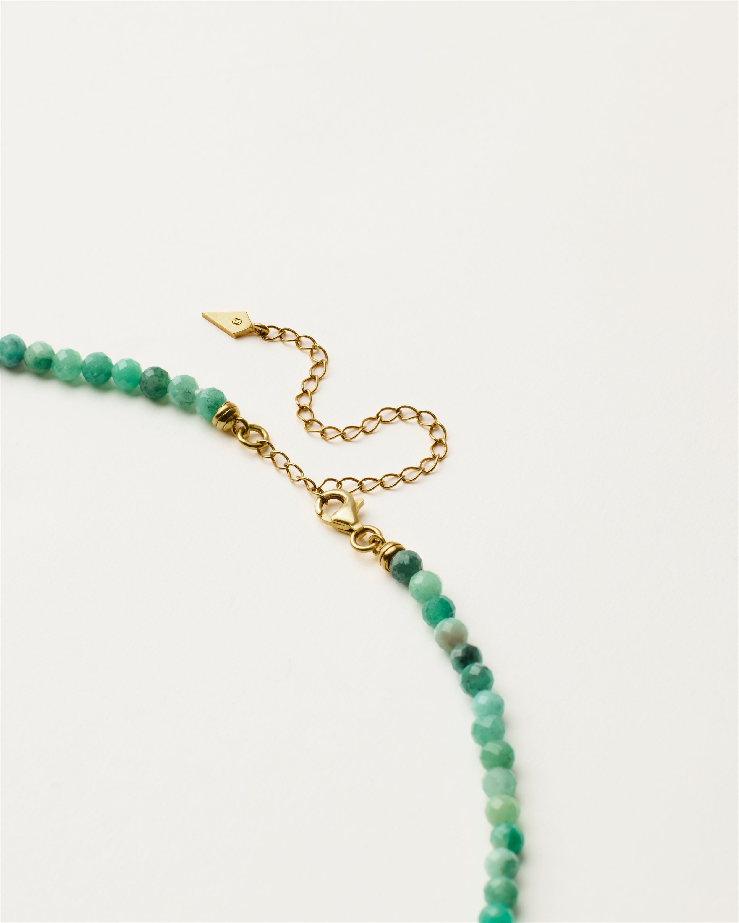 ENCARA VIRID Emerald necklace with raw polished quartz point pendant, gold 8 cm extension chain and clasp, arrowhead-shaped fantasy signature, and 4 mm faceted emerald bead strand.