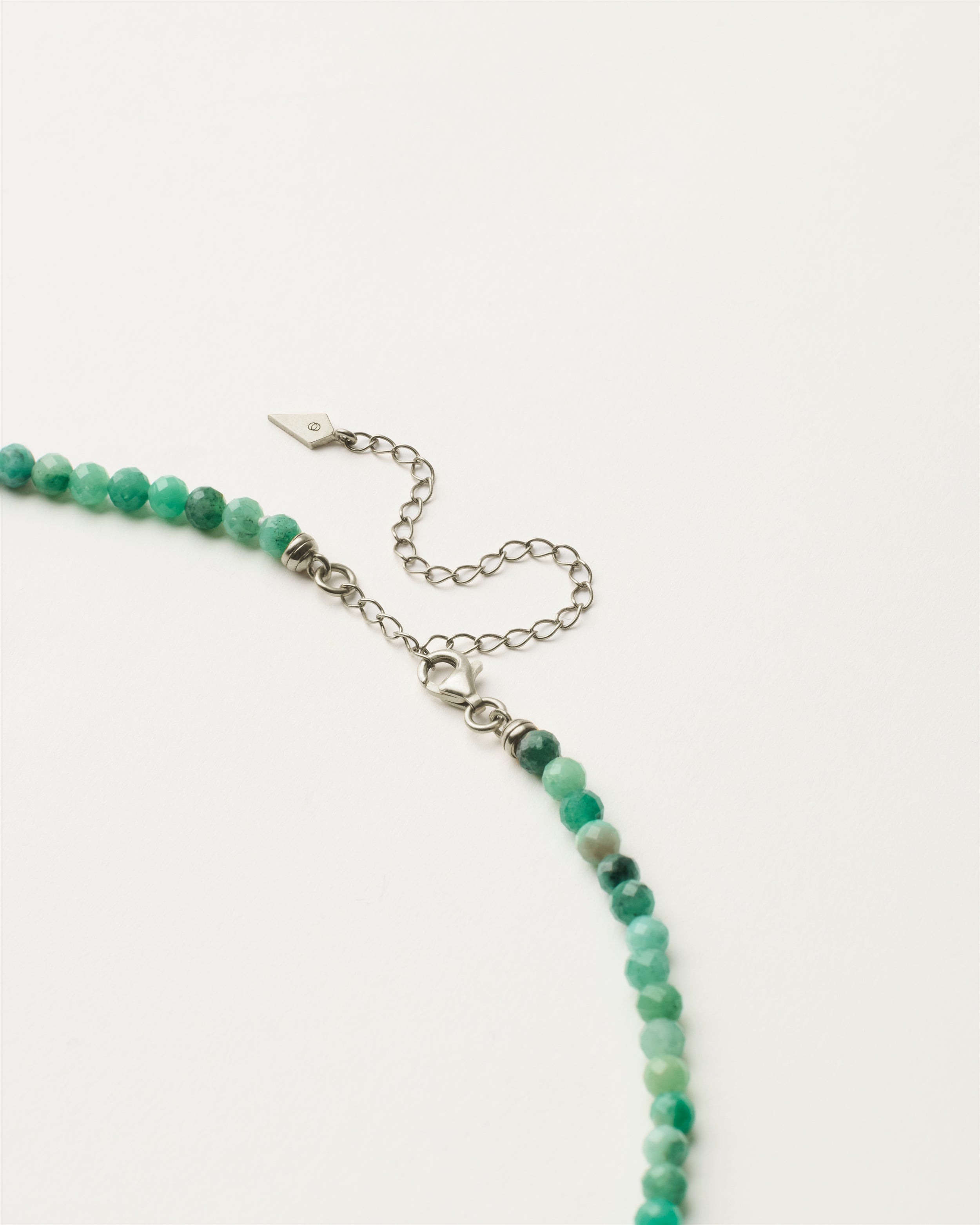 ENCARA VIRID Emerald necklace with raw polished quartz point pendant, silver 8 cm extension chain and clasp, arrowhead-shaped fantasy signature, and 4 mm faceted emerald bead strand.