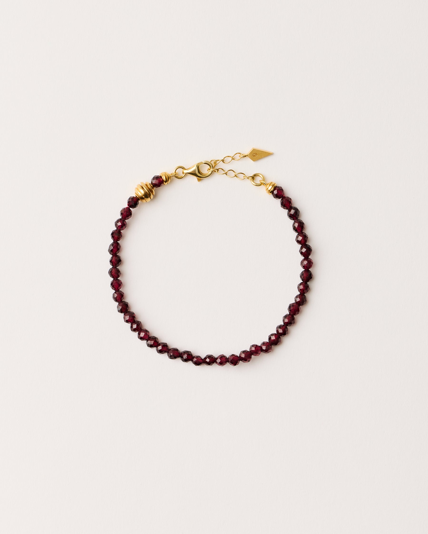 ETERNA INFERA Garnet bracelet with polished gold-plated silver spiral bead, 4 cm extension chain and clasp, arrowhead-shaped fantasy signature, and 4 mm faceted garnet bead strand.