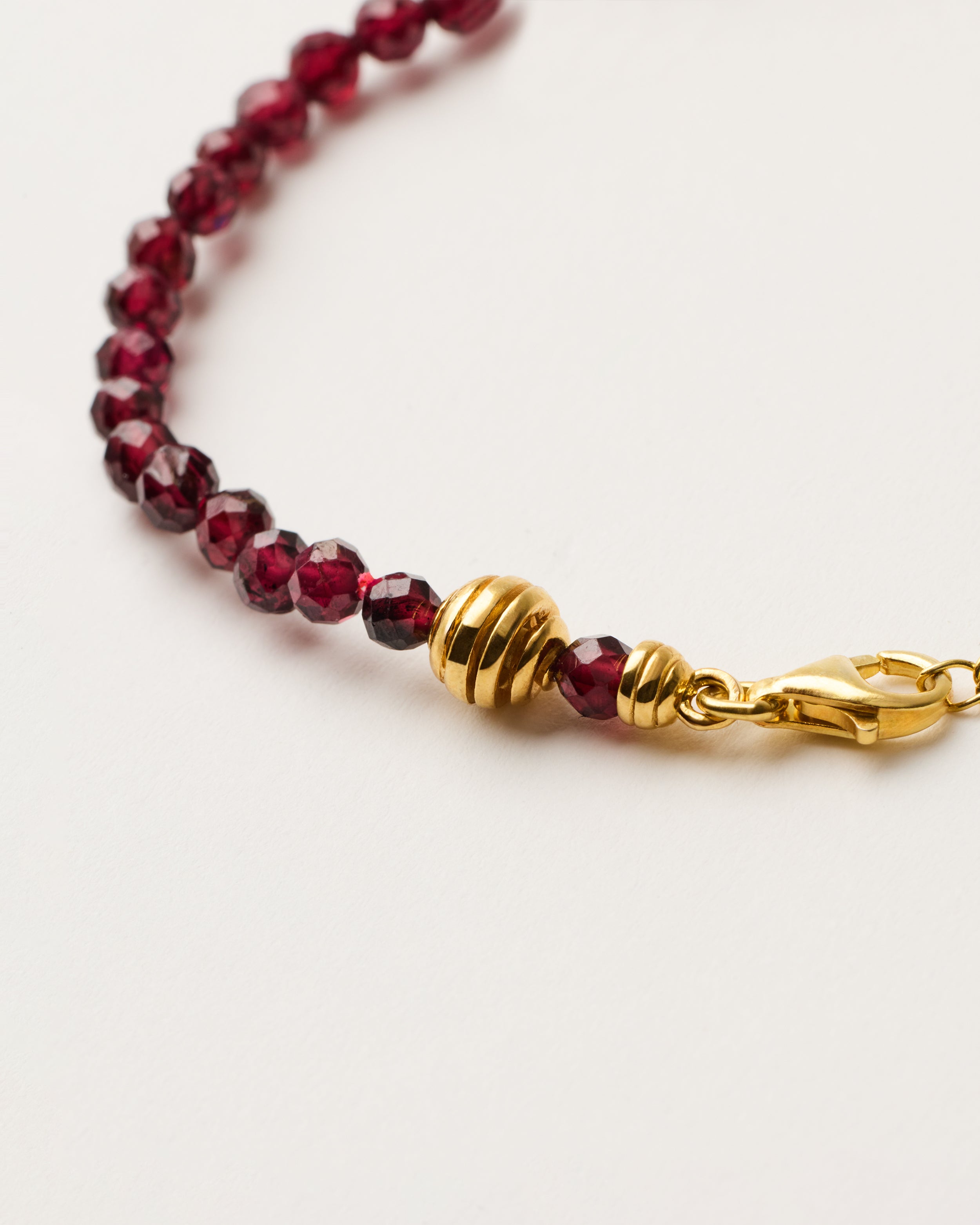 ETERNA INFERA Garnet bracelet with polished gold-plated silver spiral bead, 4 cm extension chain and clasp, arrowhead-shaped fantasy signature, and 4 mm faceted garnet bead strand.
