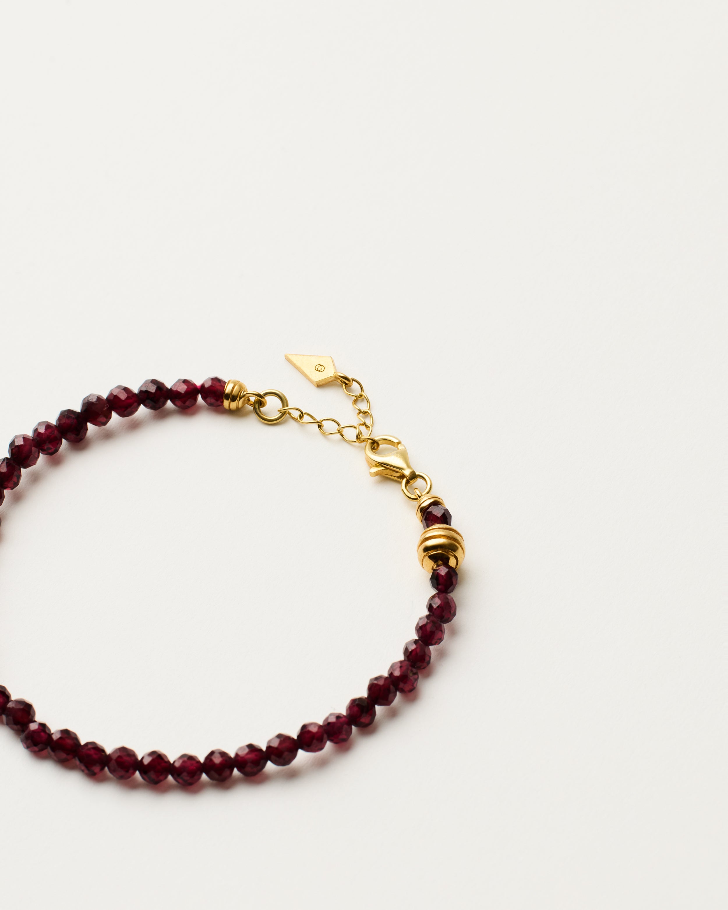 ETERNA INFERA Garnet bracelet with polished gold-plated silver spiral bead, 4 cm extension chain and clasp, arrowhead-shaped fantasy signature, and 4 mm faceted garnet bead strand.