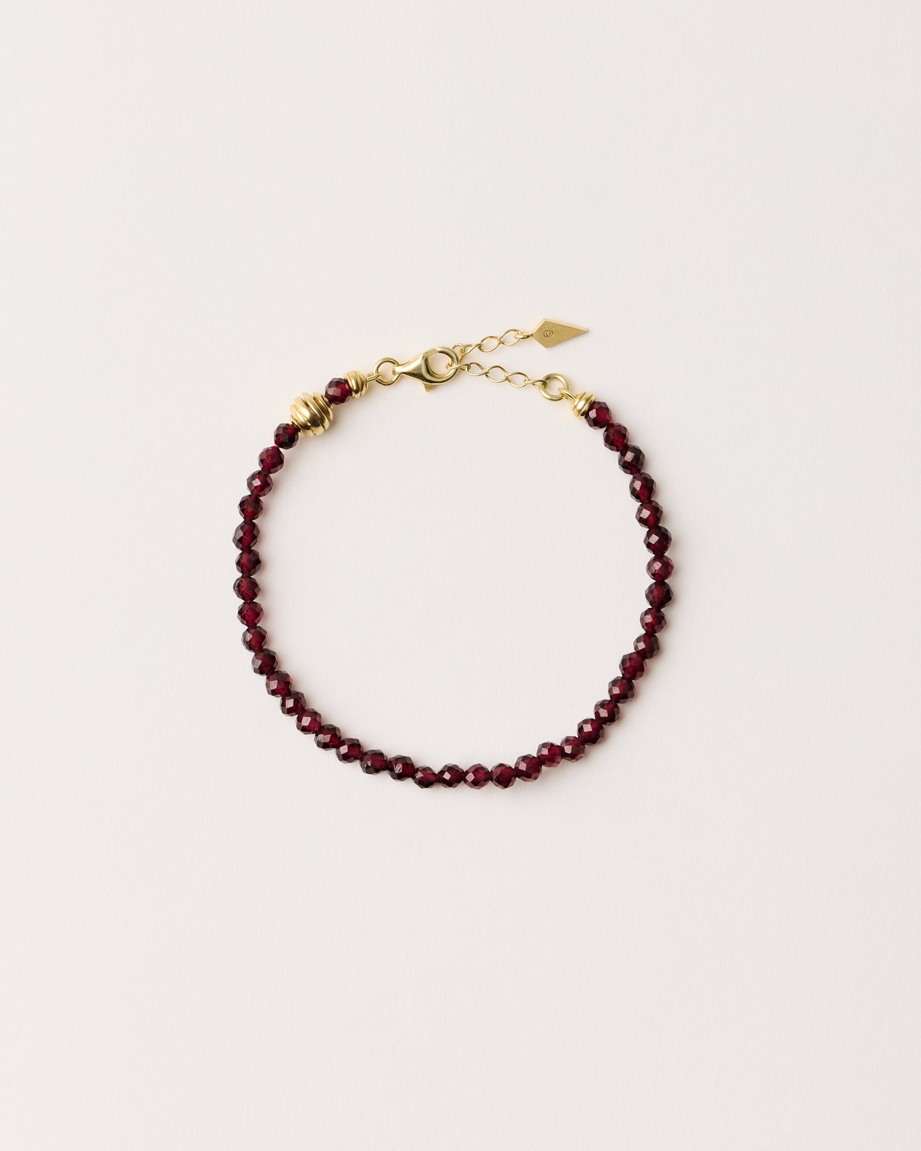 ETERNA INFERA Garnet bracelet with polished gold spiral bead, 4 cm extension chain and clasp, arrowhead-shaped fantasy signature, and 4 mm faceted garnet bead strand.