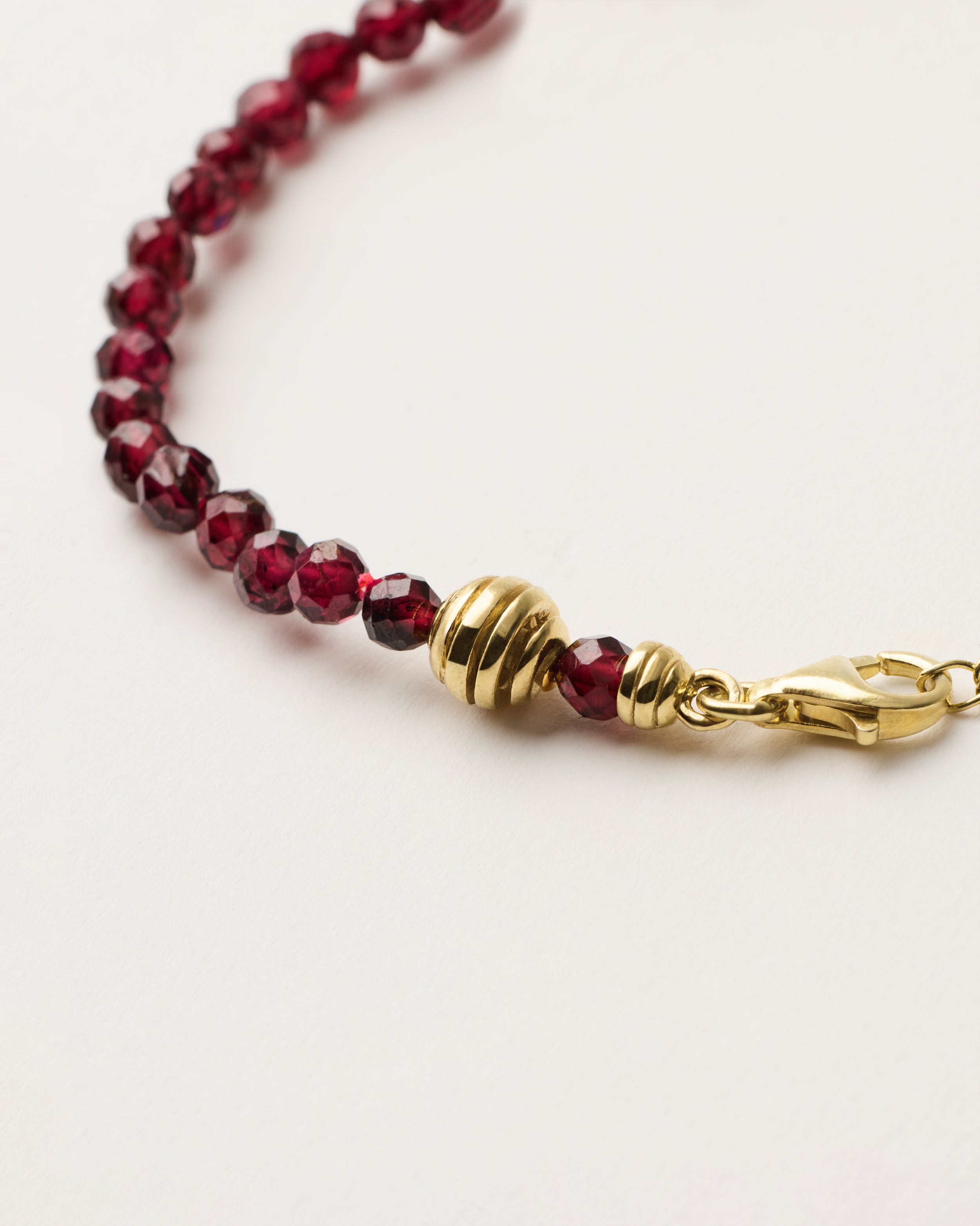 ETERNA INFERA Garnet bracelet with polished gold spiral bead, 4 cm extension chain and clasp, arrowhead-shaped fantasy signature, and 4 mm faceted garnet bead strand.