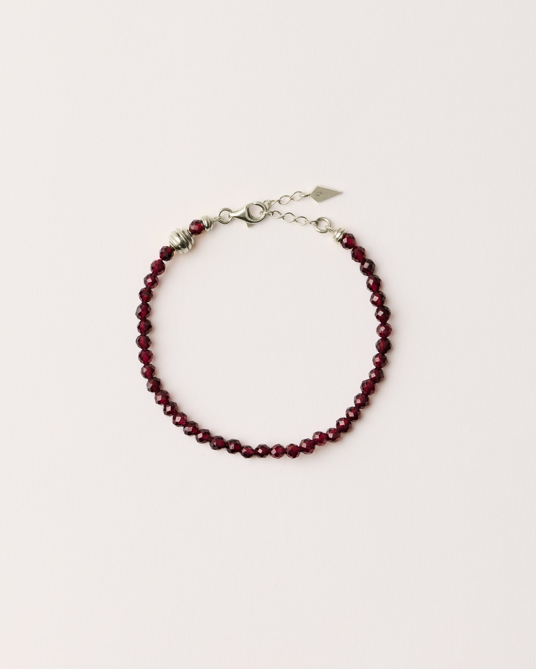 ETERNA INFERA Garnet bracelet with polished silver spiral bead, 4 cm extension chain and clasp, arrowhead-shaped fantasy signature, and 4 mm faceted garnet bead strand.