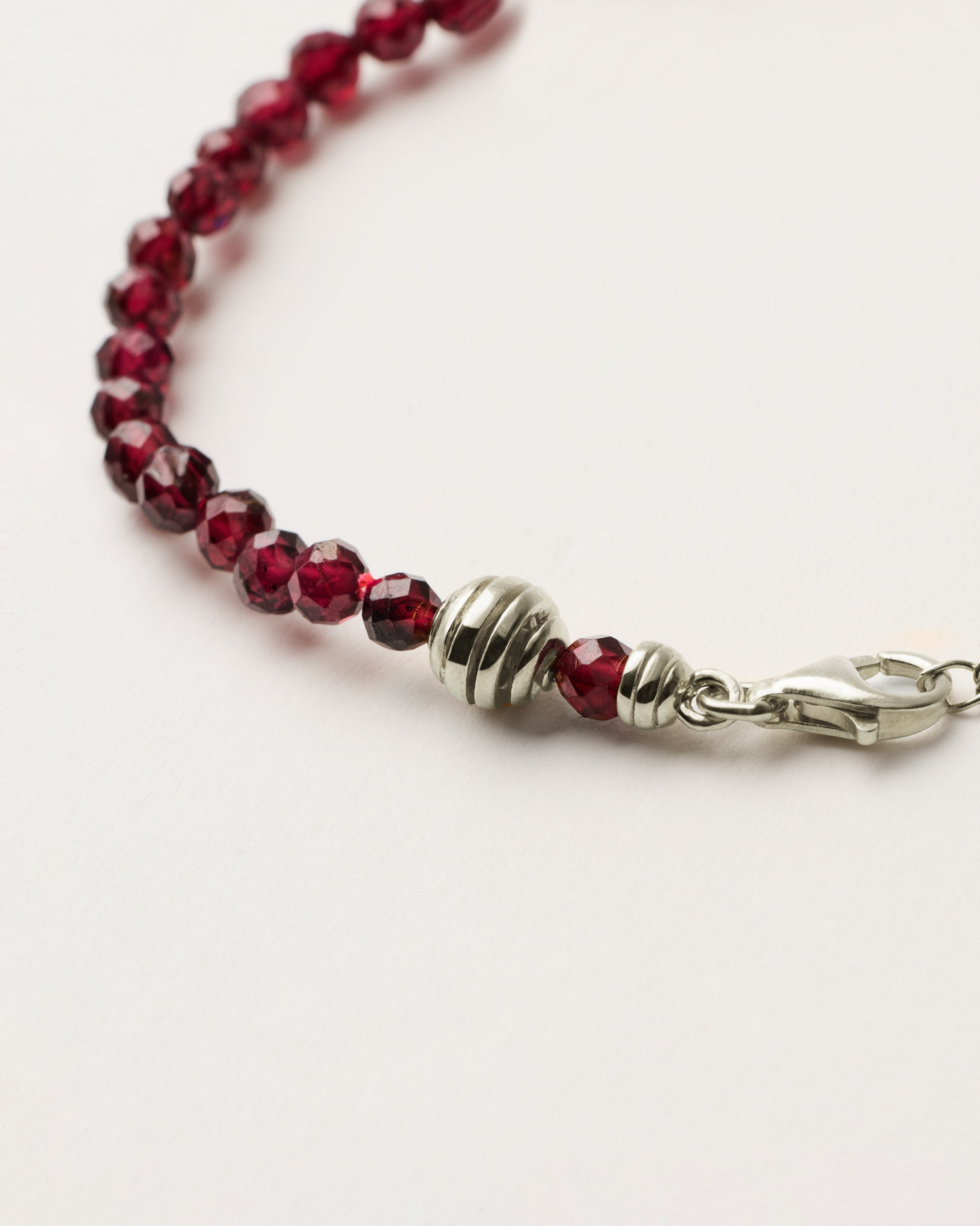ETERNA INFERA Garnet bracelet with polished silver spiral bead, 4 cm extension chain and clasp, arrowhead-shaped fantasy signature, and 4 mm faceted garnet bead strand.