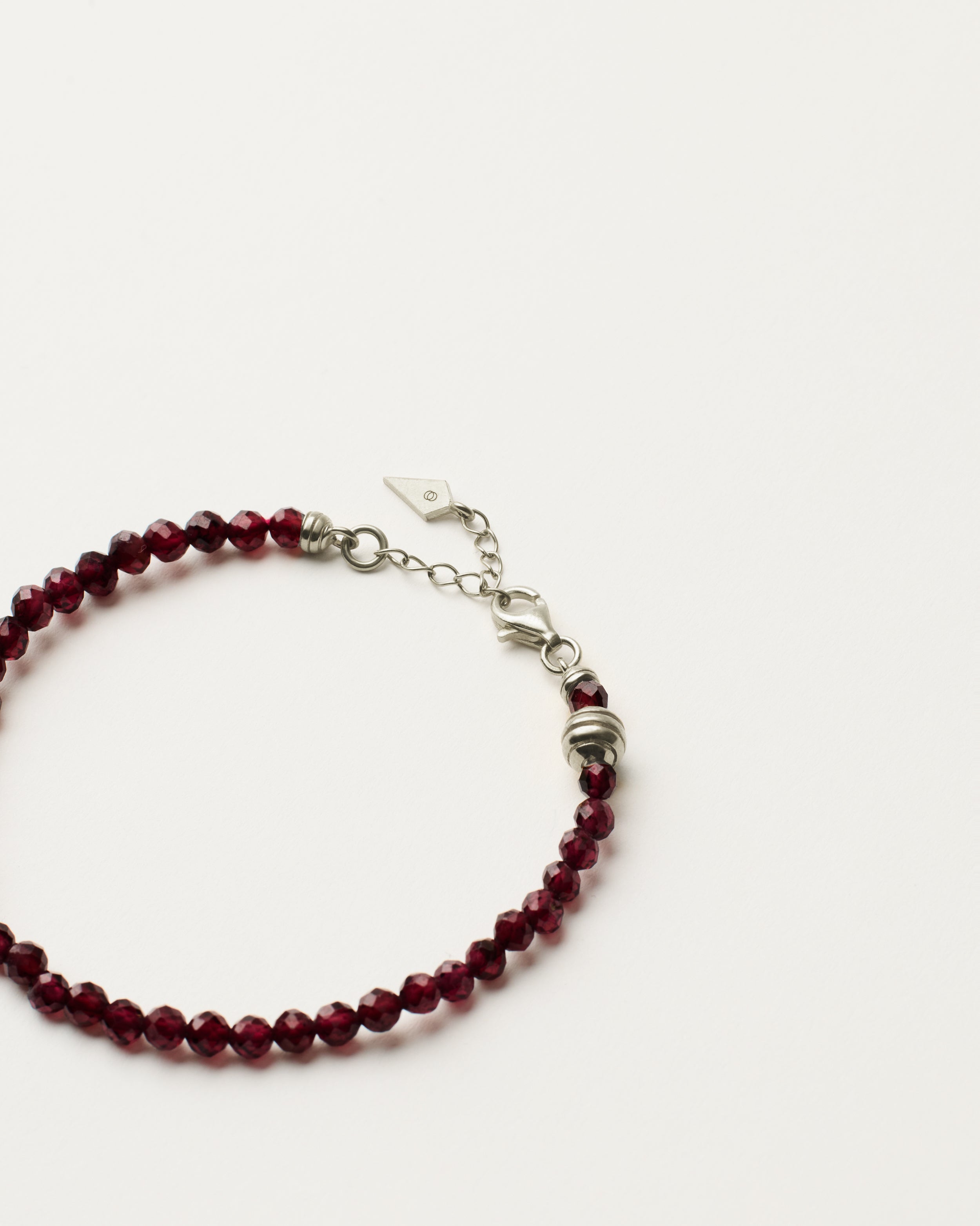 ETERNA INFERA Garnet bracelet with polished silver spiral bead, 4 cm extension chain and clasp, arrowhead-shaped fantasy signature, and 4 mm faceted garnet bead strand.