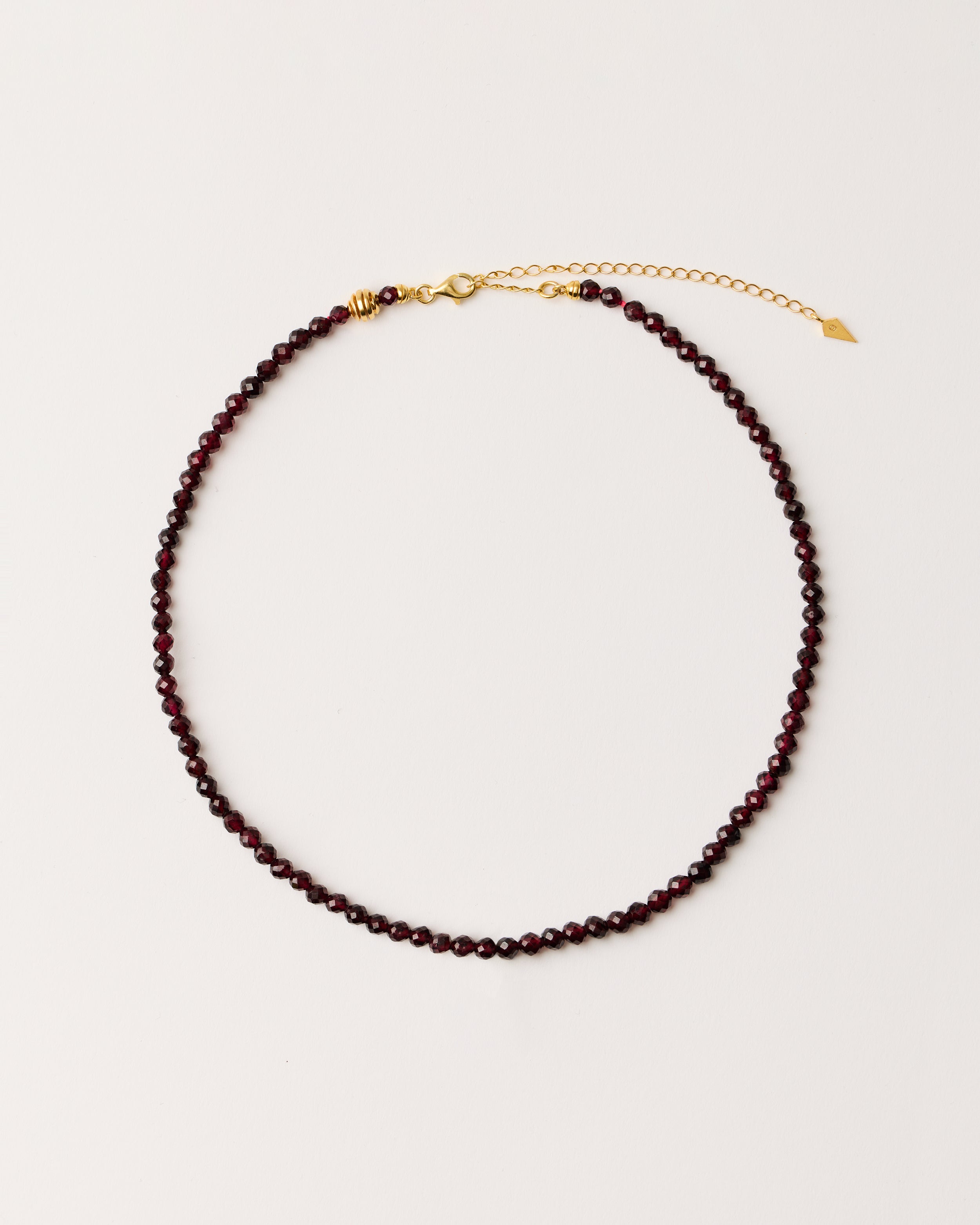 ETERNA INFERA Garnet necklace with polished gold-plated silver spiral bead, 8 cm extension chain and clasp, arrowhead-shaped fantasy signature, and 4 mm faceted garnet bead strand.