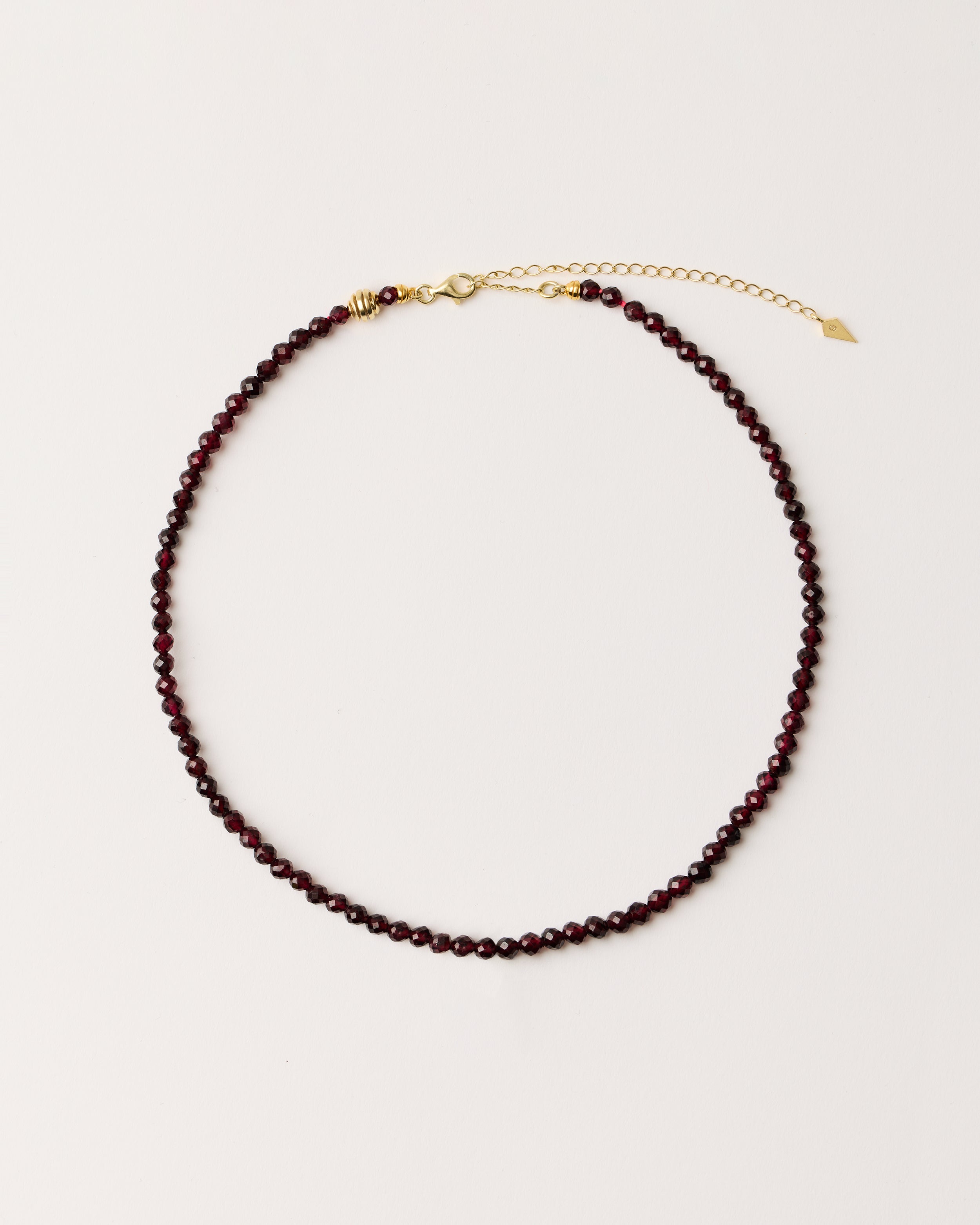 ETERNA INFERA Garnet necklace with polished gold spiral bead, 8 cm extension chain and clasp, arrowhead-shaped fantasy signature, and 4 mm faceted garnet bead strand.