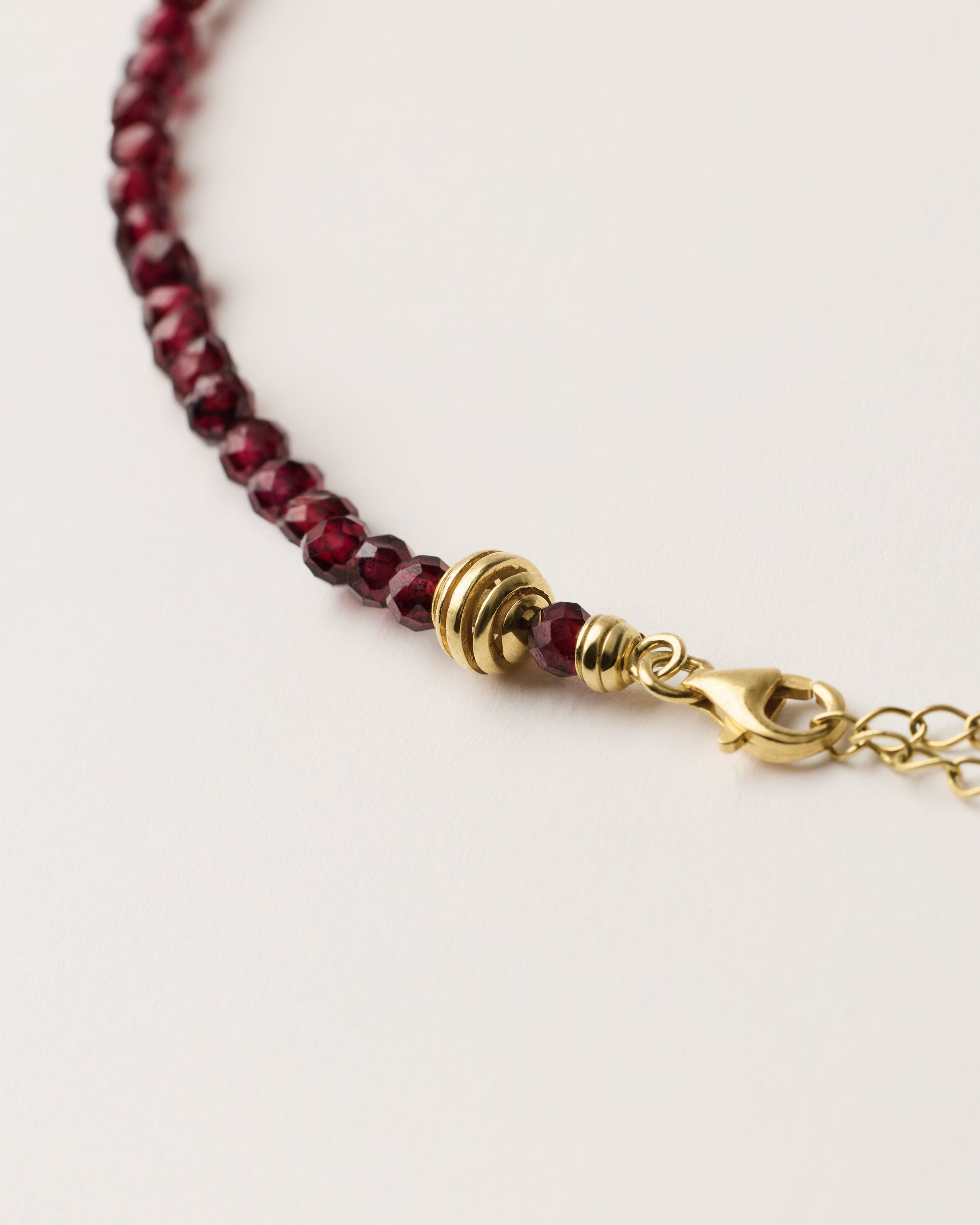 ETERNA INFERA Garnet necklace with polished gold spiral bead, 8 cm extension chain and clasp, arrowhead-shaped fantasy signature, and 4 mm faceted garnet bead strand.