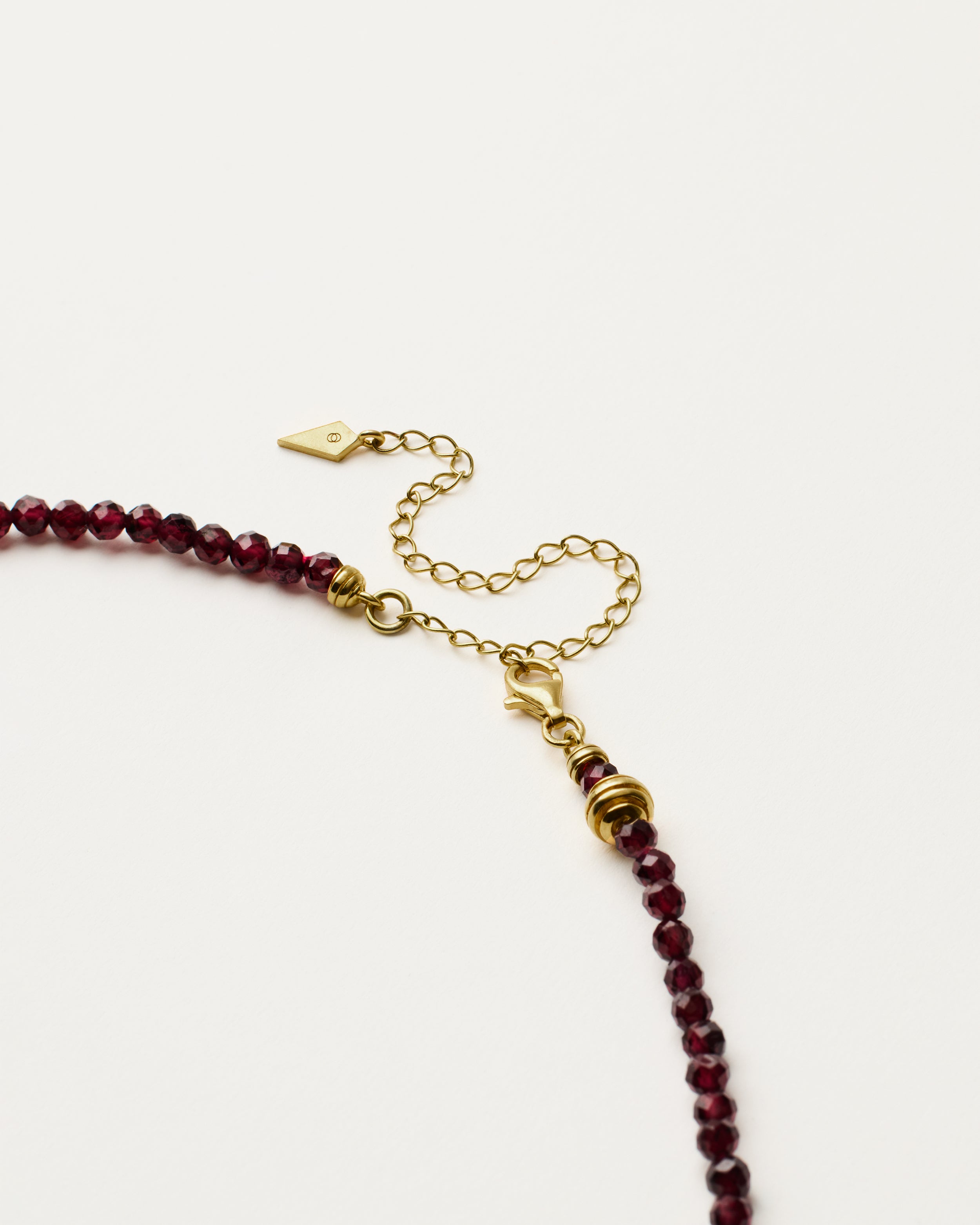 ETERNA INFERA Garnet necklace with polished gold spiral bead, 8 cm extension chain and clasp, arrowhead-shaped fantasy signature, and 4 mm faceted garnet bead strand.