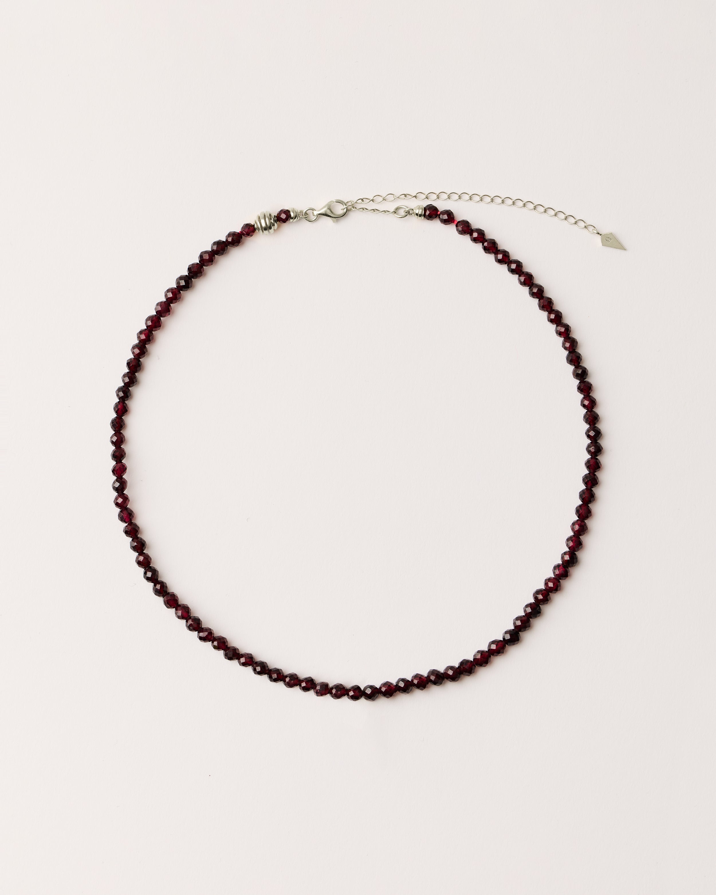 ETERNA INFERA Garnet necklace with polished silver spiral bead, 8 cm extension chain and clasp, arrowhead-shaped fantasy signature, and 4 mm faceted garnet bead strand.