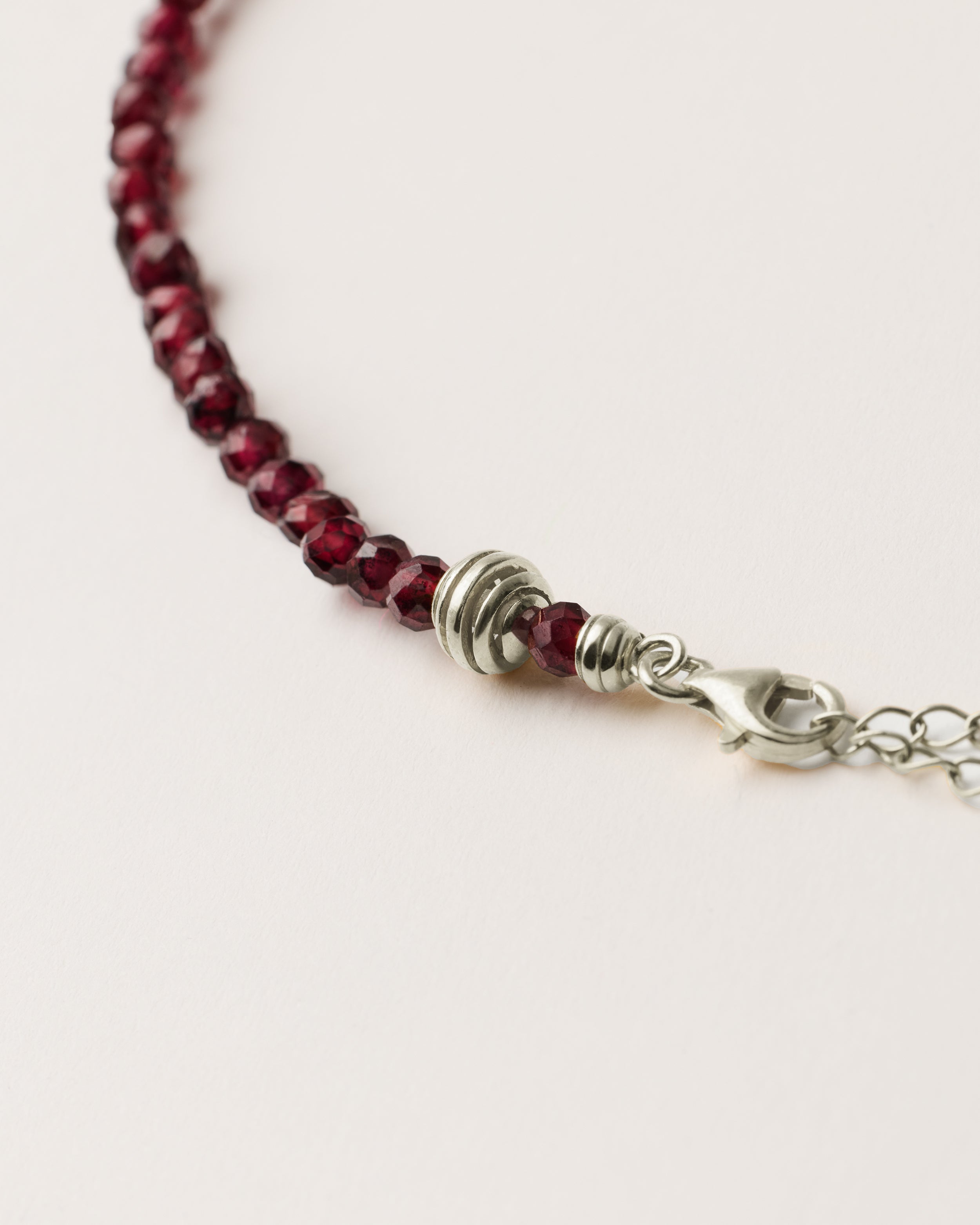 ETERNA INFERA Garnet necklace with polished silver spiral bead, 8 cm extension chain and clasp, arrowhead-shaped fantasy signature, and 4 mm faceted garnet bead strand.