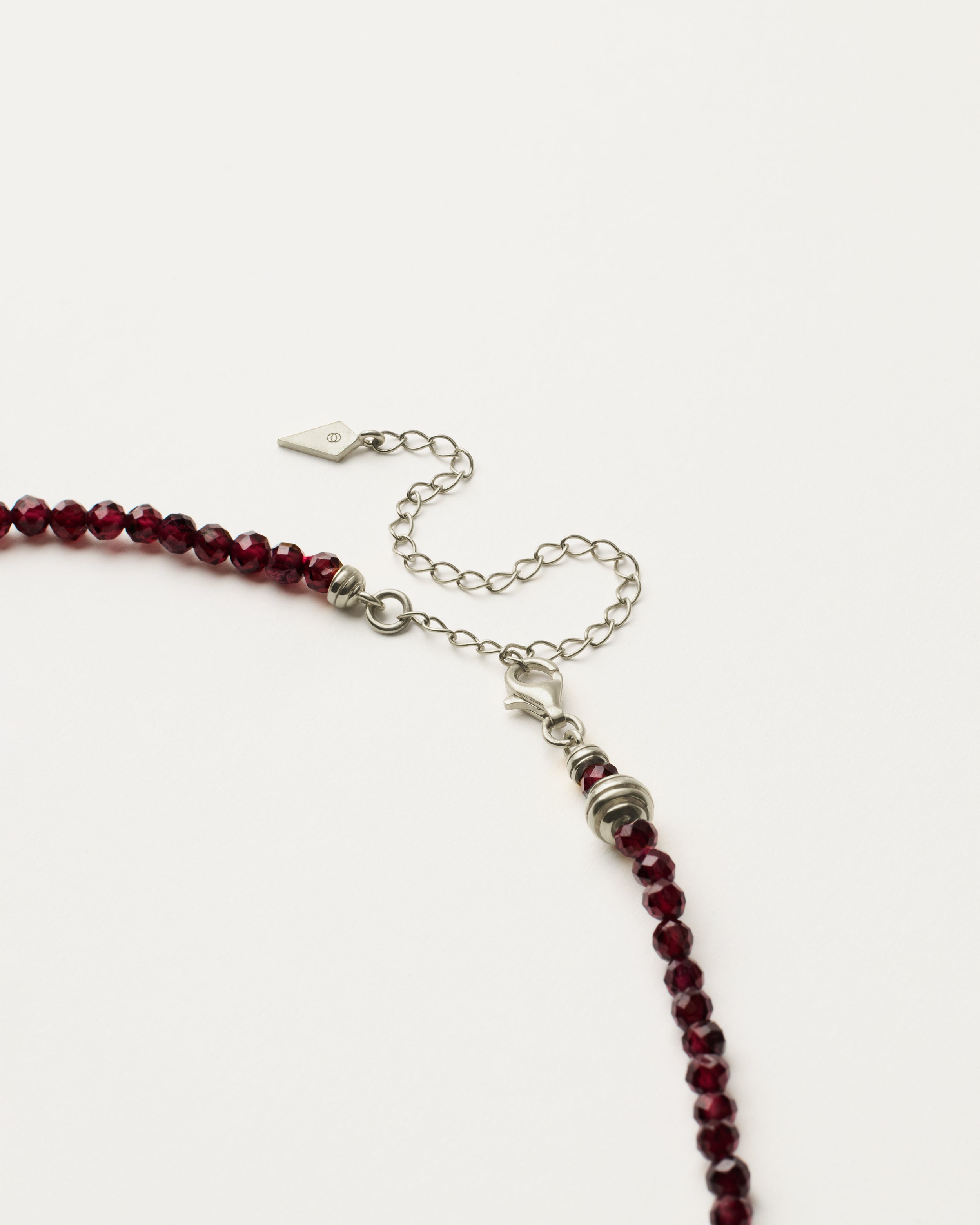 ETERNA INFERA Garnet necklace with polished silver spiral bead, 8 cm extension chain and clasp, arrowhead-shaped fantasy signature, and 4 mm faceted garnet bead strand.