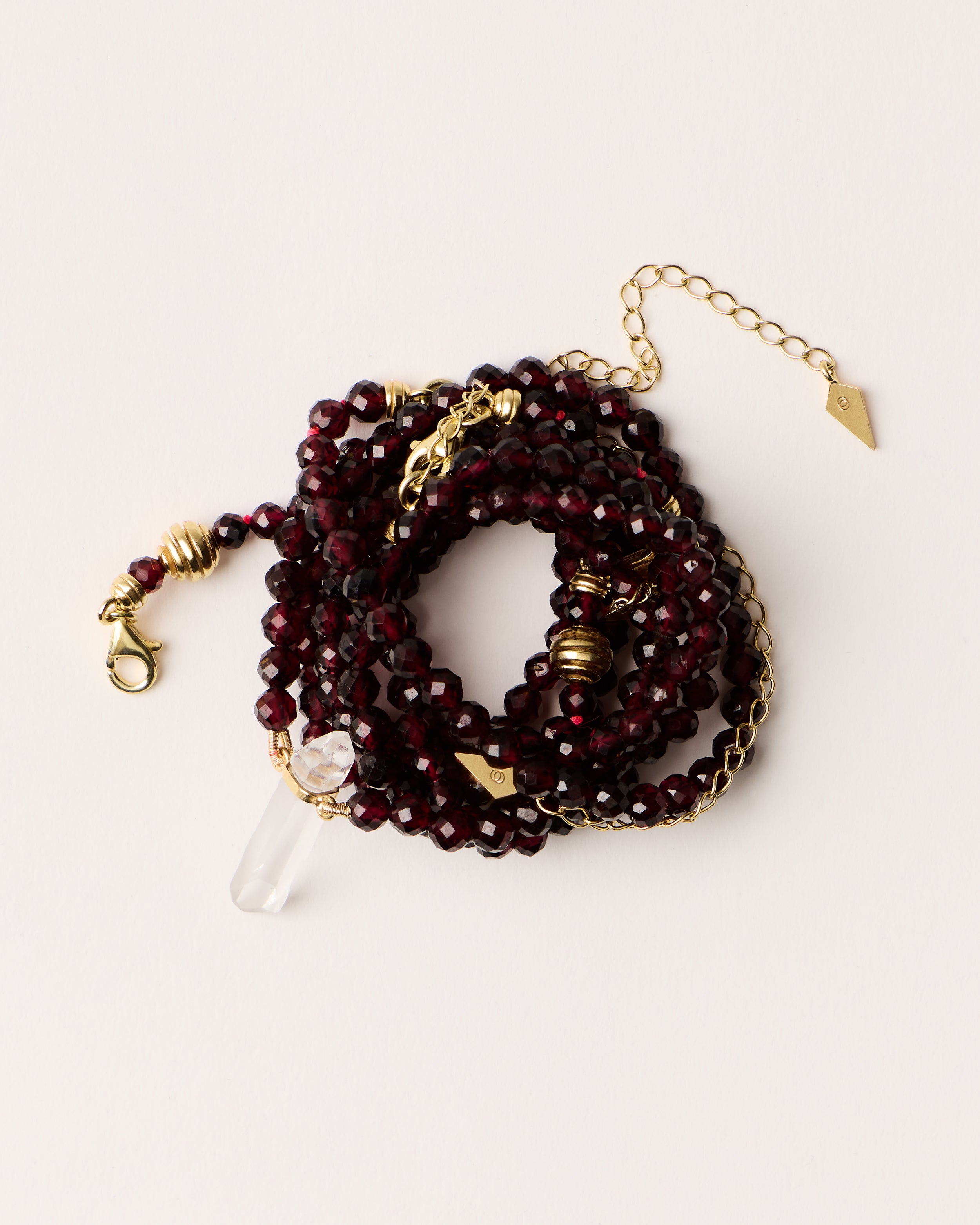 ENCARA / ETERNA INFERA Garnet necklaces and bracelet with polished gold spiral bead, extension chain and clasp, arrowhead-shaped fantasy signature, and 4 mm faceted garnet bead strand and raw polished quartz point pendant.