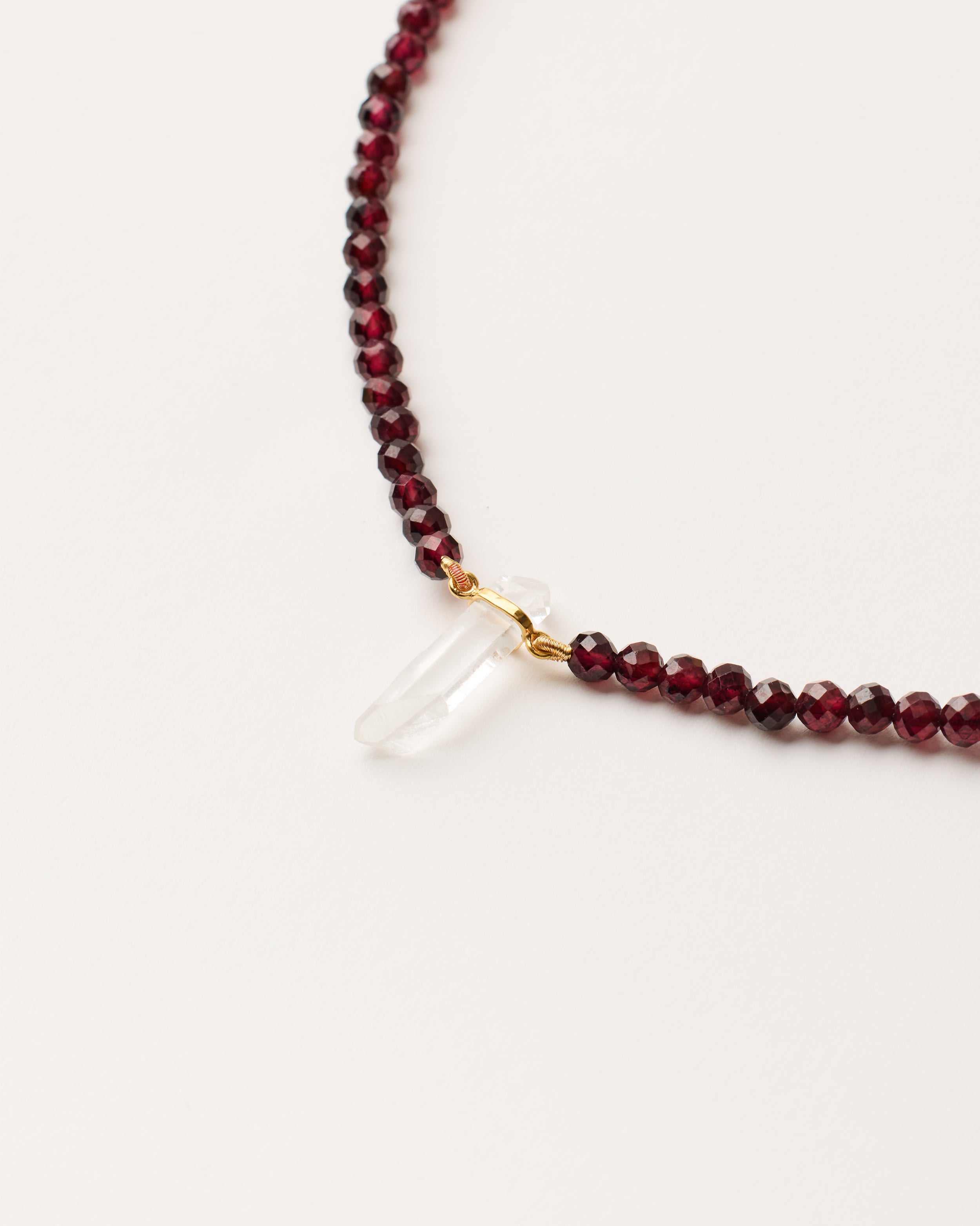 ENCARA INFERA Garnet necklace with raw polished quartz point pendant, gold-plated silver 8 cm extension chain and clasp, arrowhead-shaped fantasy signature, and 4 mm faceted garnet bead strand.