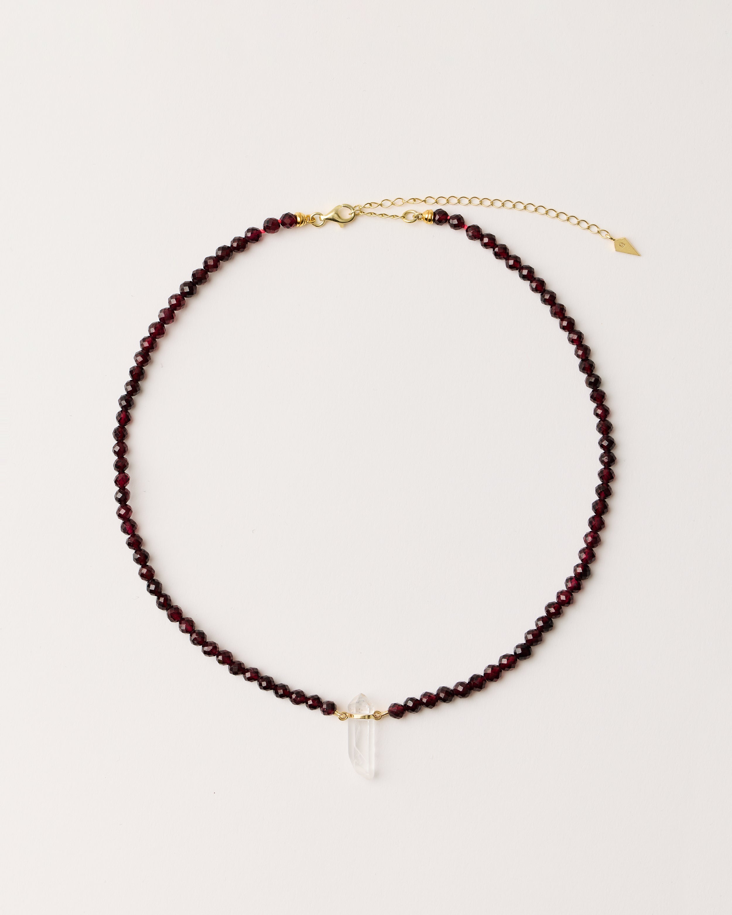 ENCARA INFERA Garnet necklace with raw polished quartz point pendant, gold 8 cm extension chain and clasp, arrowhead-shaped fantasy signature, and 4 mm faceted garnet bead strand.