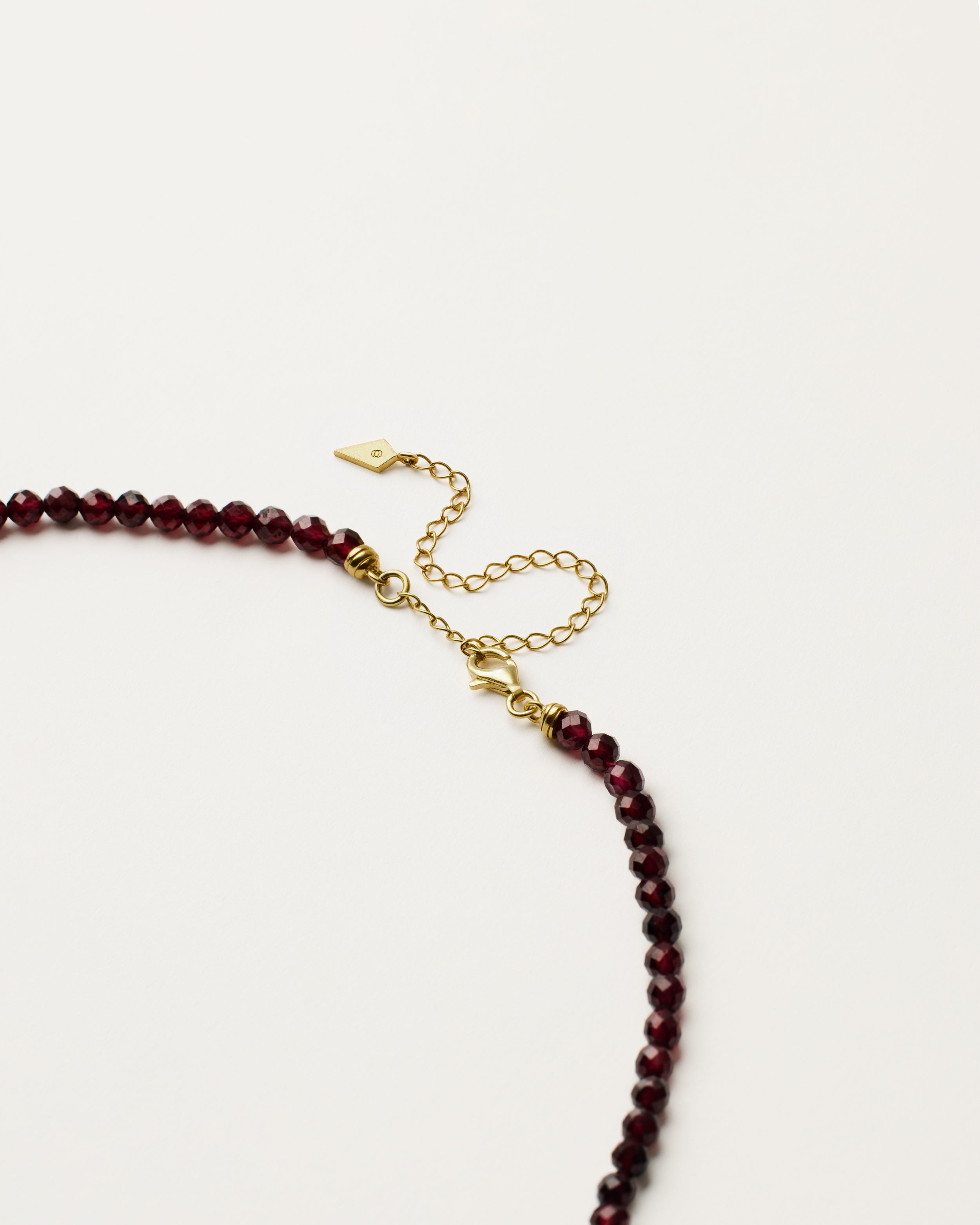 ENCARA INFERA Garnet necklace with raw polished quartz point pendant, gold 8 cm extension chain and clasp, arrowhead-shaped fantasy signature, and 4 mm faceted garnet bead strand.
