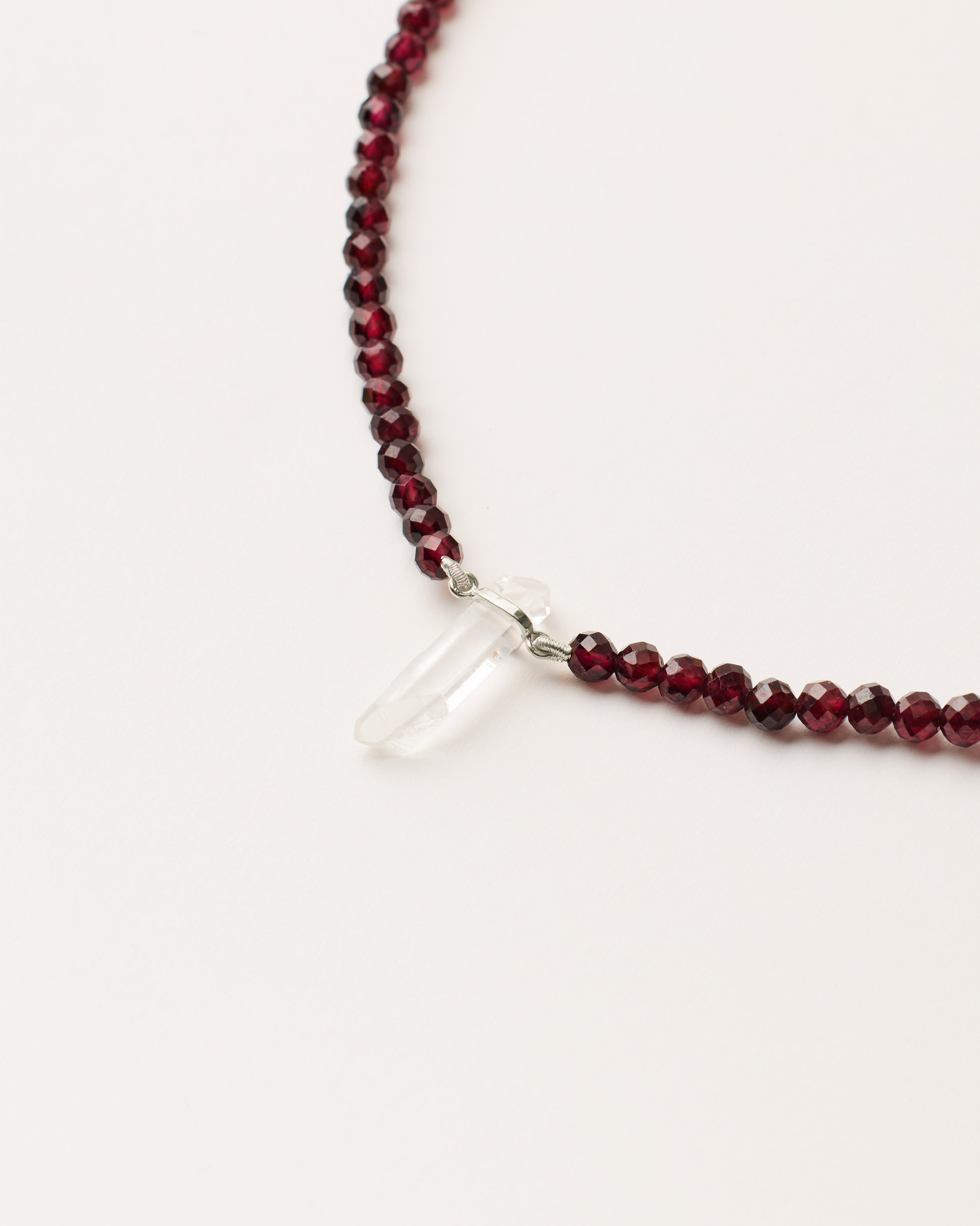 ENCARA INFERA Garnet necklace with raw polished quartz point pendant, silver 8 cm extension chain and clasp, arrowhead-shaped fantasy signature, and 4 mm faceted garnet bead strand.