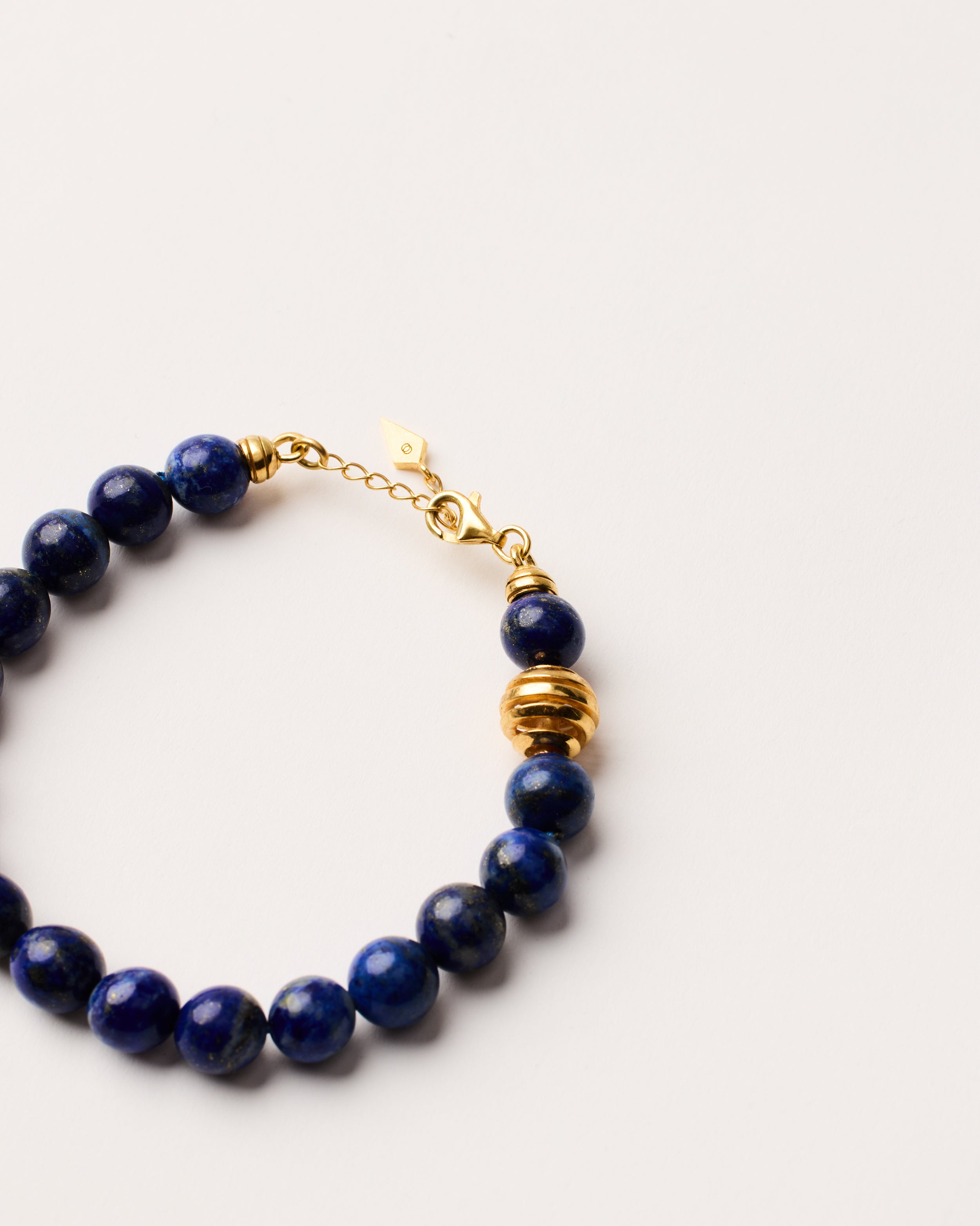 ETERNA NOCTA Lapis Lazuli necklace with polished gold-plated silver spiral bead, 8 cm extension chain and clasp, arrowhead-shaped fantasy signature, and 8 mm faceted lazurite bead strand.