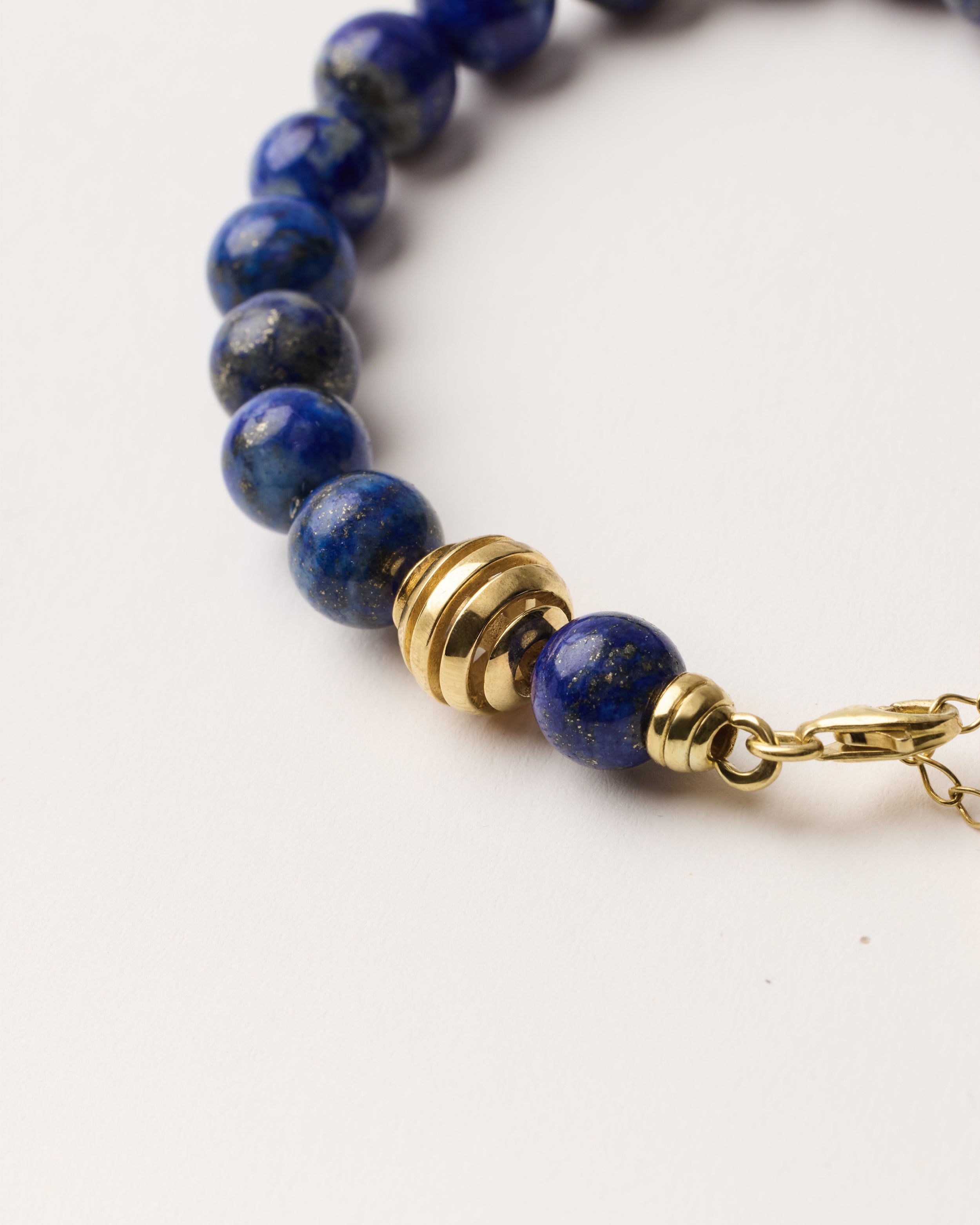 ETERNA NOCTA Lapis Lazuli necklace with polished gold spiral bead, 8 cm extension chain and clasp, arrowhead-shaped fantasy signature, and 8 mm faceted lazurite bead strand.