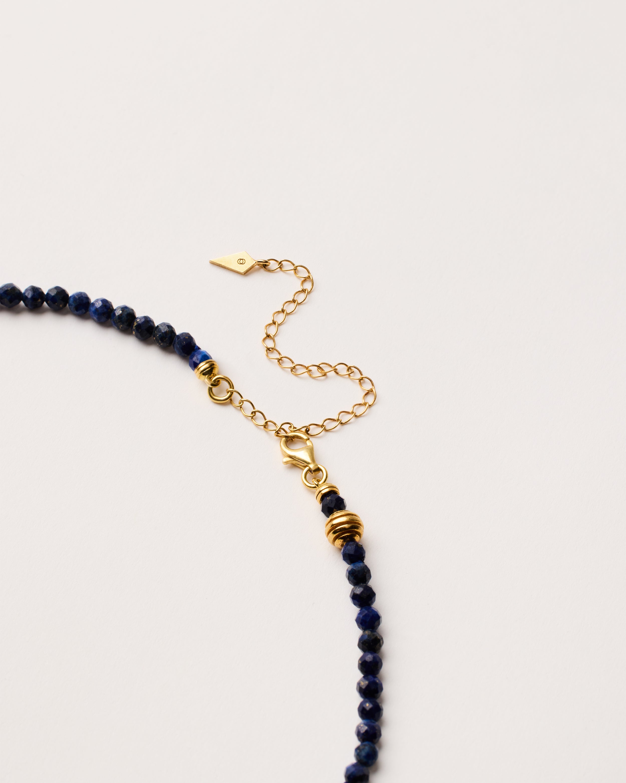 ENCARA NOCTA Lapis Lazuli necklace with raw polished quartz point pendant, gold-plated silver 8 cm extension chain and clasp, arrowhead-shaped fantasy signature, and 4 mm faceted lazurite bead strand.