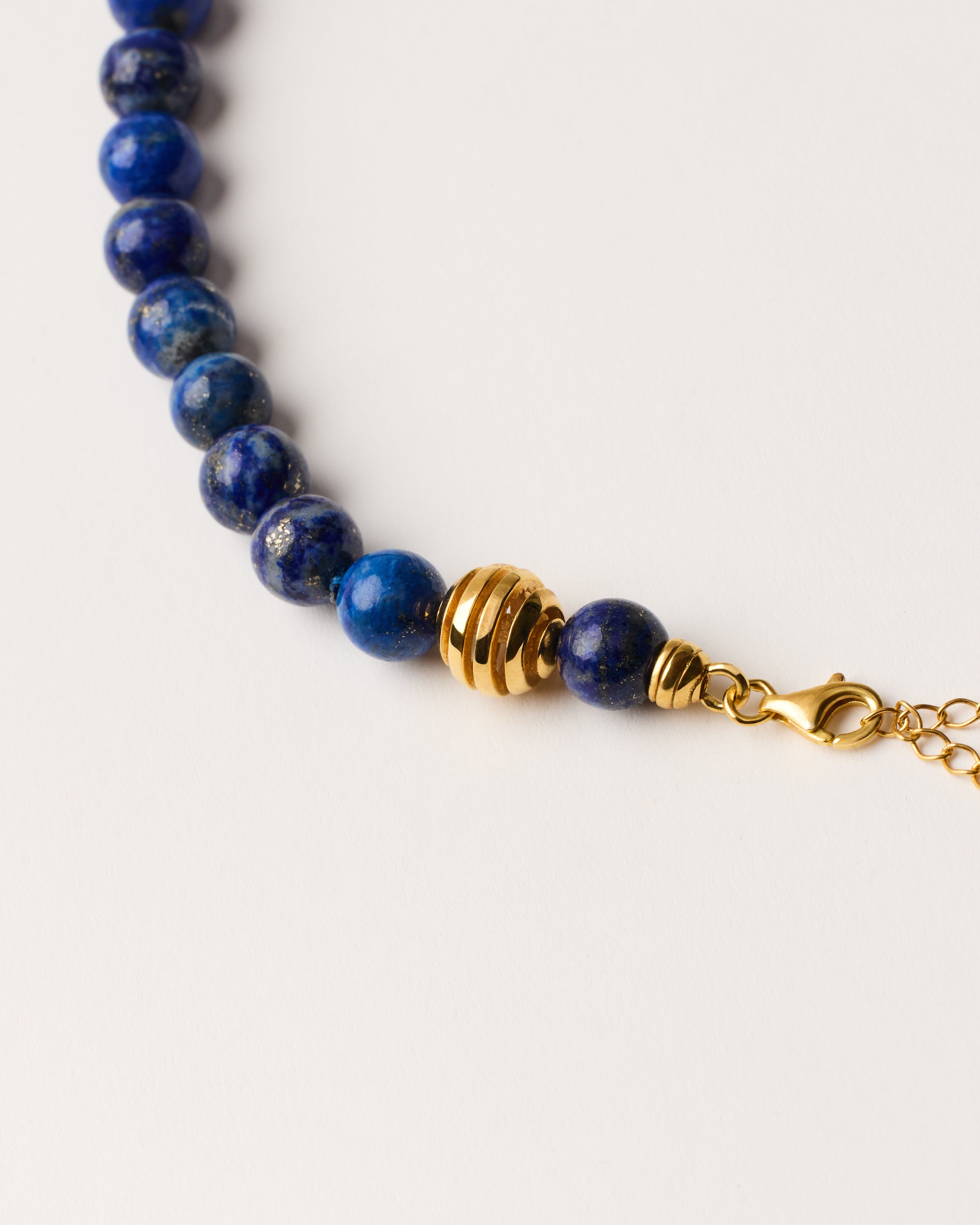 ETERNA NOCTA Lapis Lazuli necklace with polished gold-plated silver spiral bead, 8 cm extension chain and clasp, arrowhead-shaped fantasy signature, and 8 mm faceted lazurite bead strand.