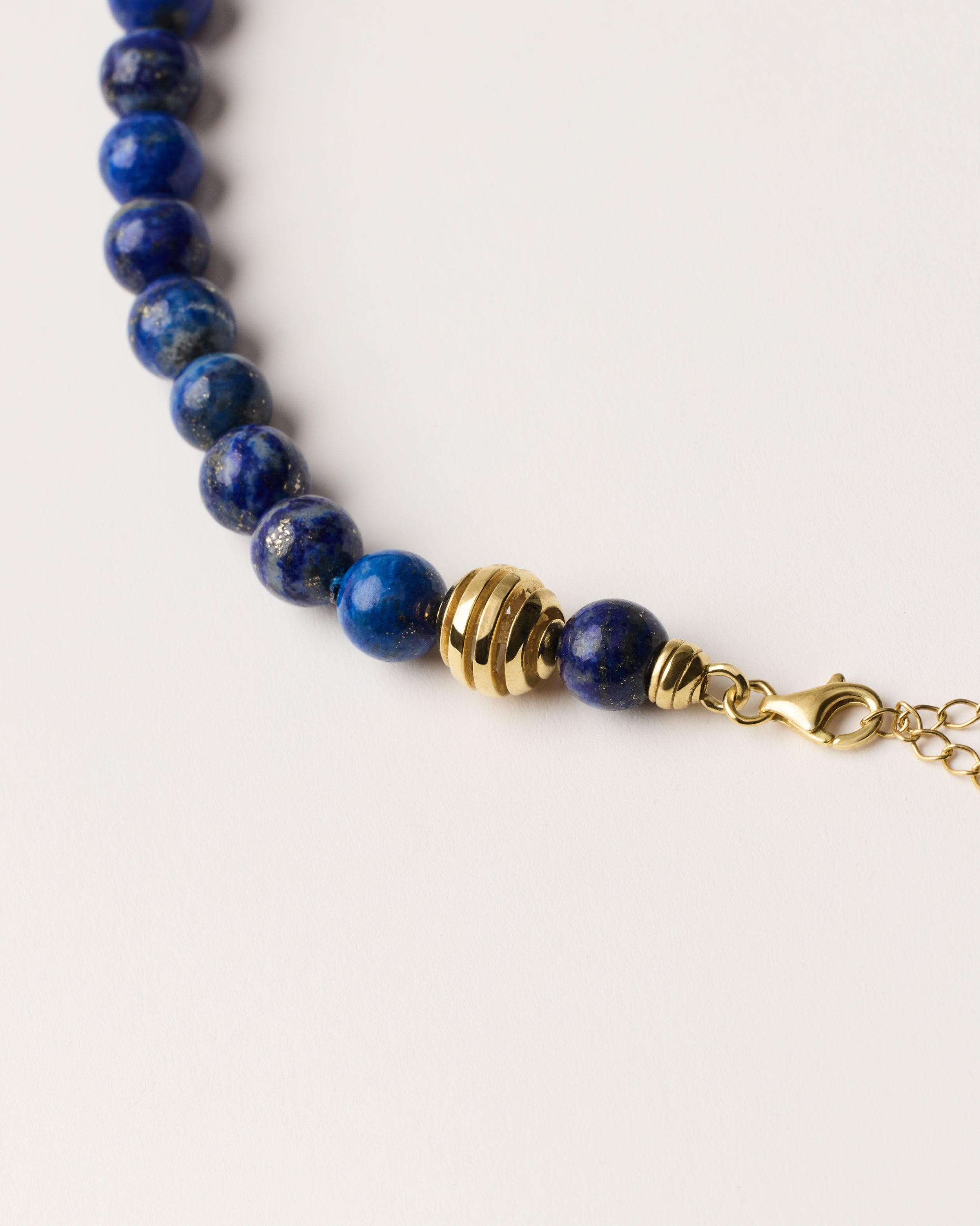 ETERNA NOCTA Lapis Lazuli necklace with polished gold spiral bead, 8 cm extension chain and clasp, arrowhead-shaped fantasy signature, and 8 mm faceted lazurite bead strand.