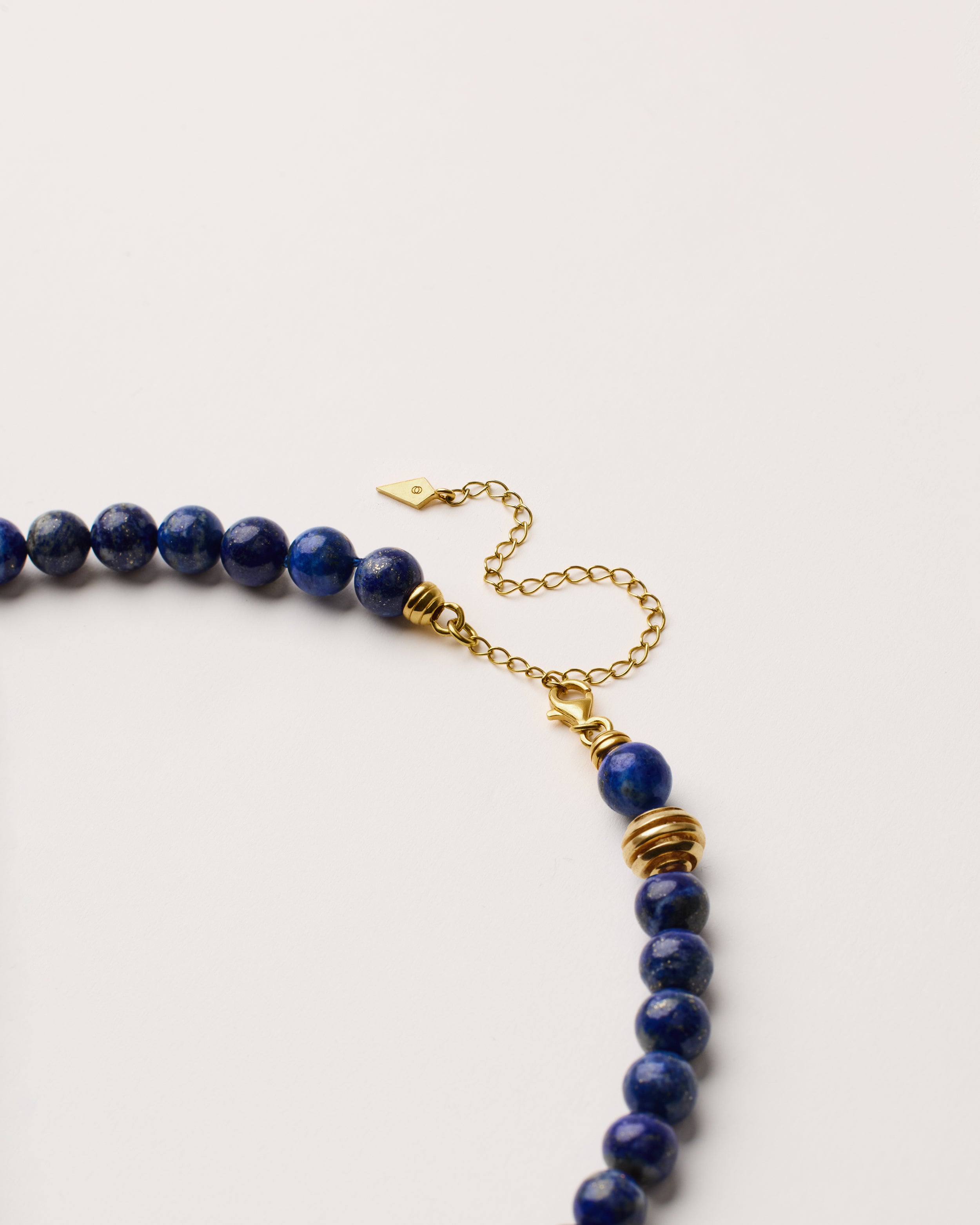 ETERNA NOCTA Lapis Lazuli necklace with polished gold spiral bead, 8 cm extension chain and clasp, arrowhead-shaped fantasy signature, and 8 mm faceted lazurite bead strand.