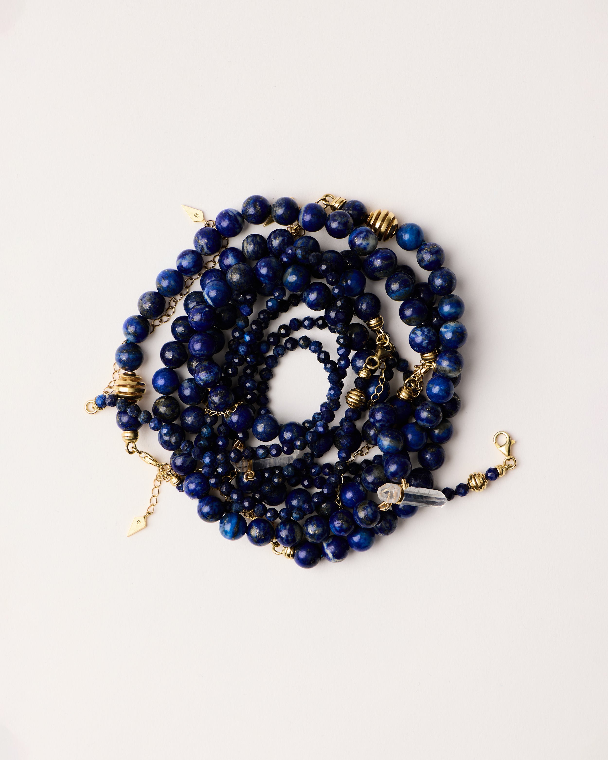 ENCARA / ETERNA NOCTA Lapis Lazuli necklaces and bracelet with polished gold spiral bead, extension chain and clasp, arrowhead-shaped fantasy signature, 8 mm and 4 mm faceted lazurite bead strand and raw polished quartz point pendant.