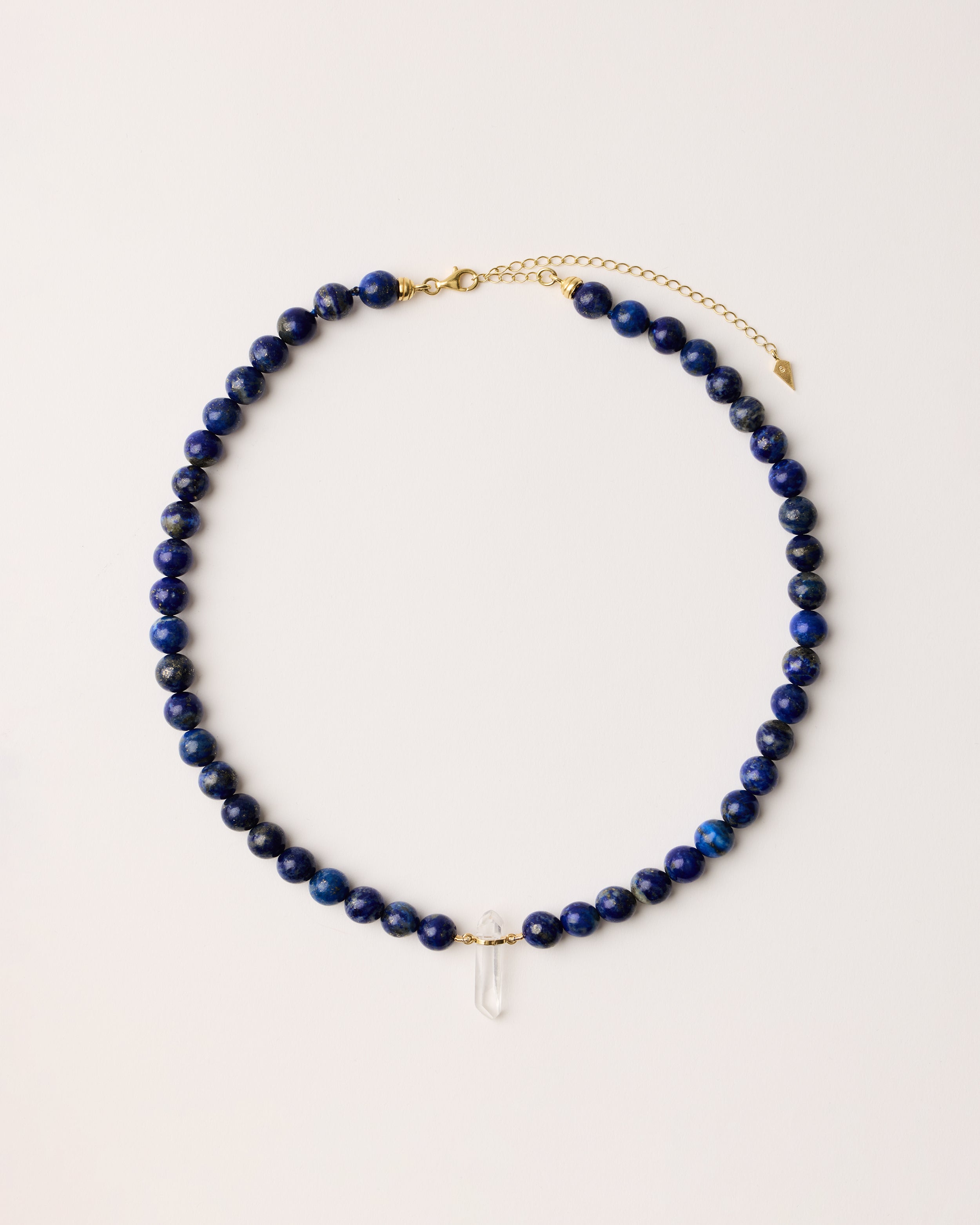 ENCARA NOCTA Lapis Lazuli necklace with raw polished quartz point pendant, gold 8 cm extension chain and clasp, arrowhead-shaped fantasy signature, and 8 mm faceted lazurite bead strand.