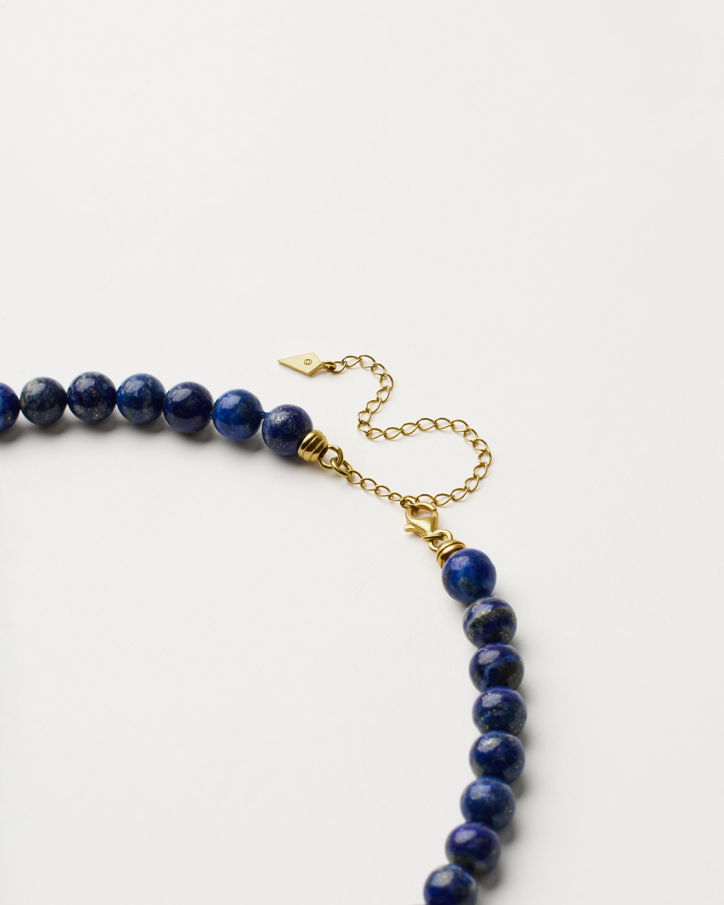 ENCARA NOCTA Lapis Lazuli necklace with raw polished quartz point pendant, gold 8 cm extension chain and clasp, arrowhead-shaped fantasy signature, and 8 mm faceted lazurite bead strand.