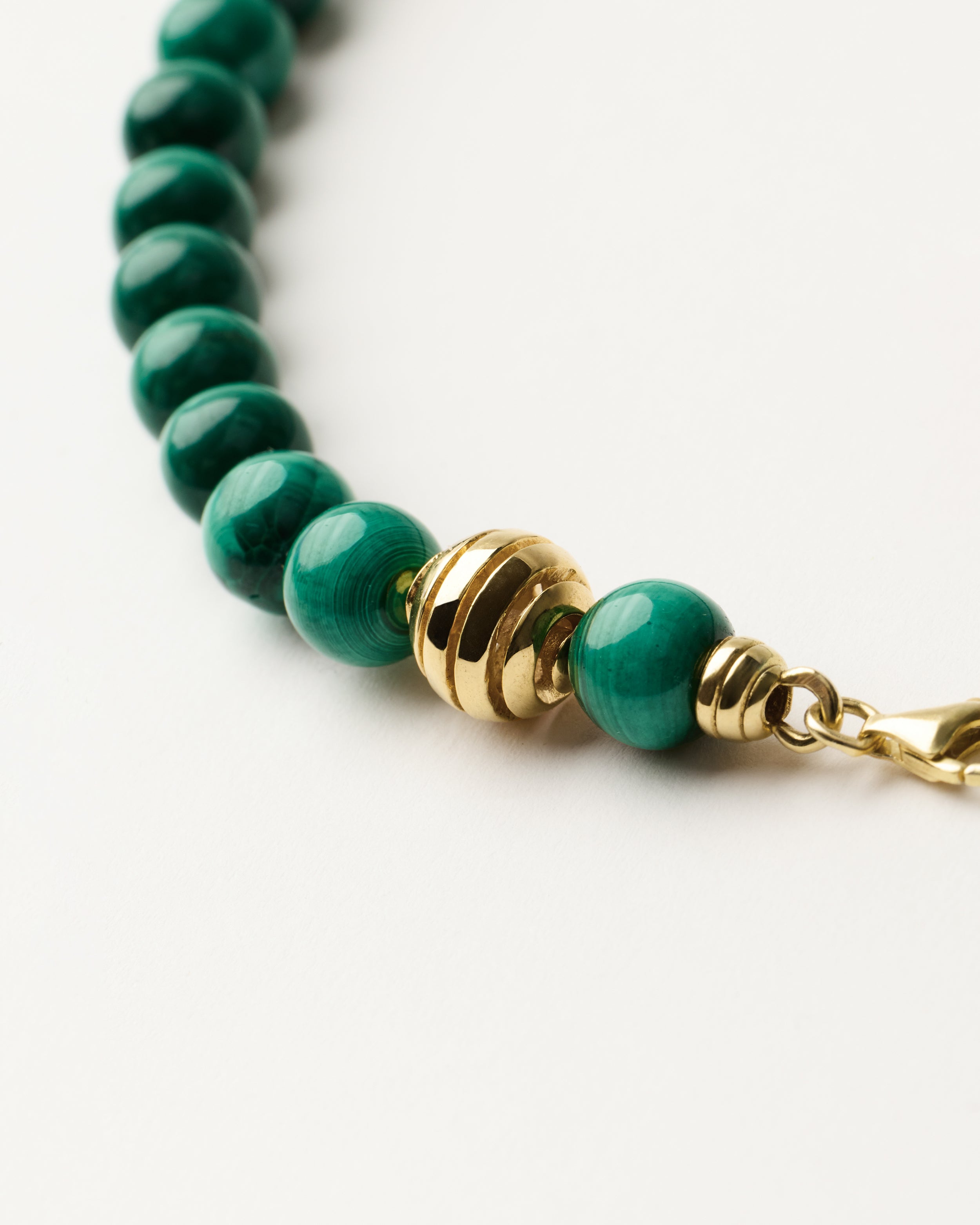 ETERNA VERDAN Malachite necklace with polished gold spiral bead, 8 cm extension chain and clasp, arrowhead-shaped fantasy signature, and 8 mm faceted malachite bead strand.