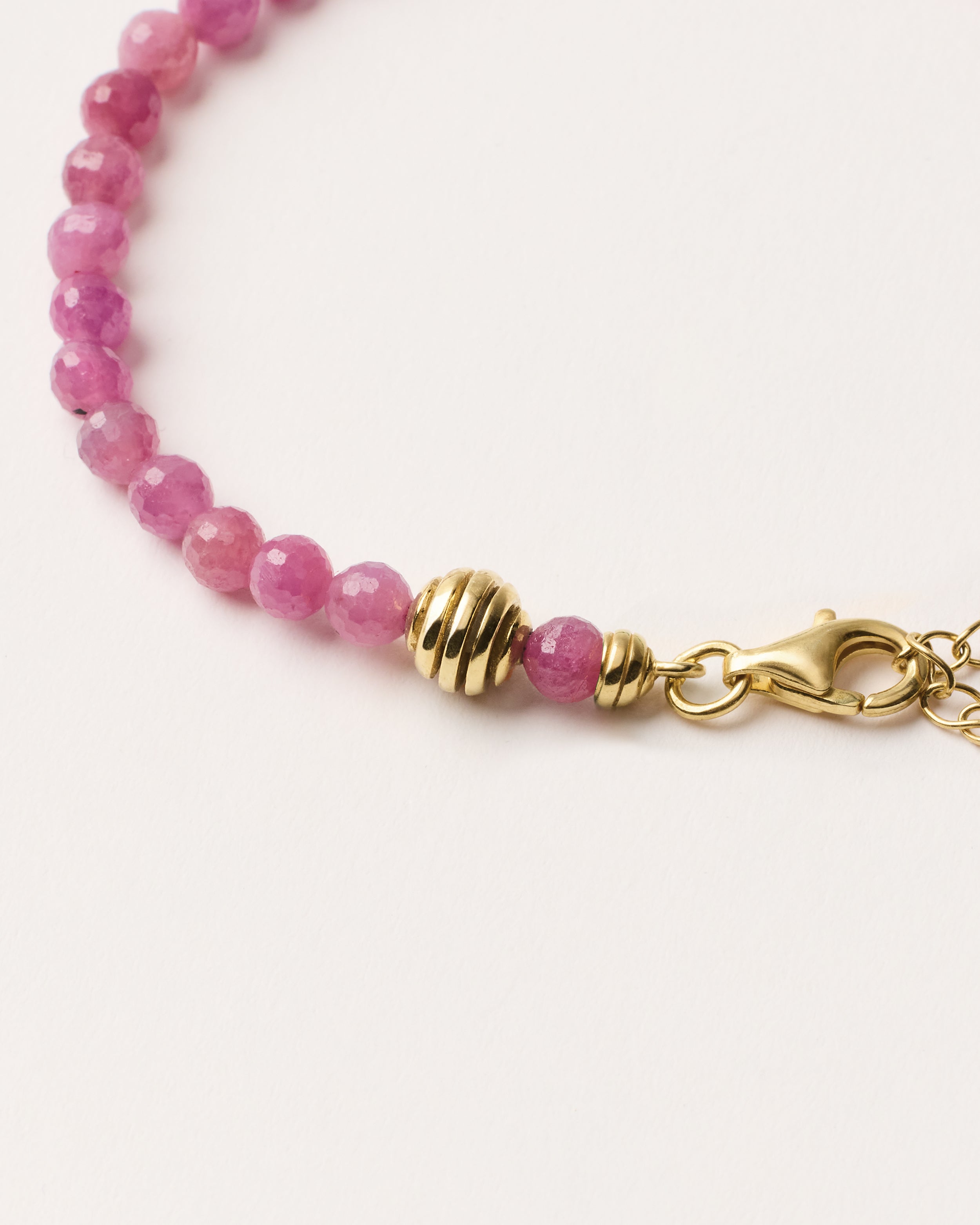 ETERNA CARMES Ruby bracelet with polished gold spiral bead, 4 cm extension chain and clasp, arrowhead-shaped fantasy signature, and 4 mm faceted ruby bead strand.