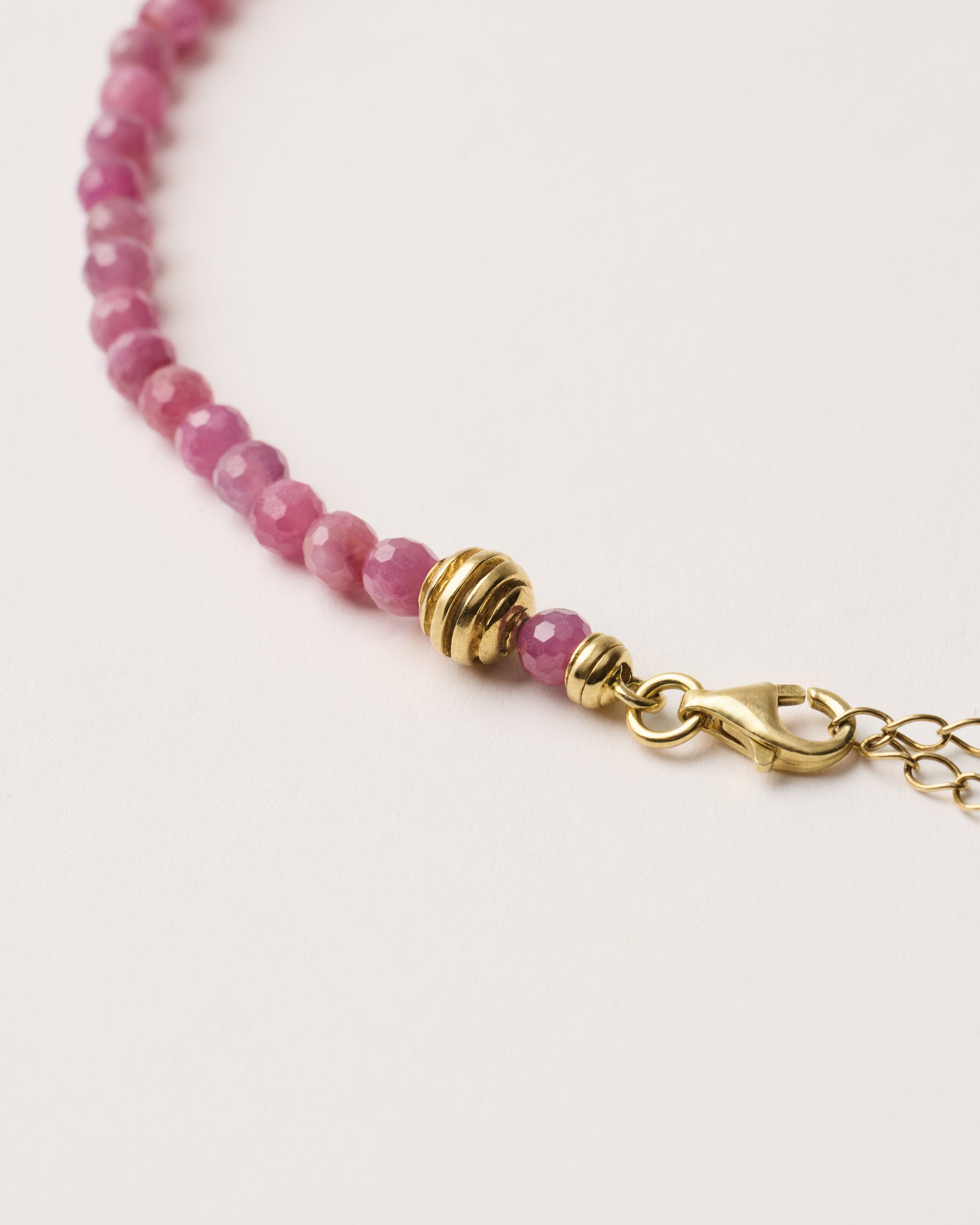 ETERNA CARMES Ruby necklace with polished gold spiral bead, 8 cm extension chain and clasp, arrowhead-shaped fantasy signature, and 4 mm faceted ruby bead strand.