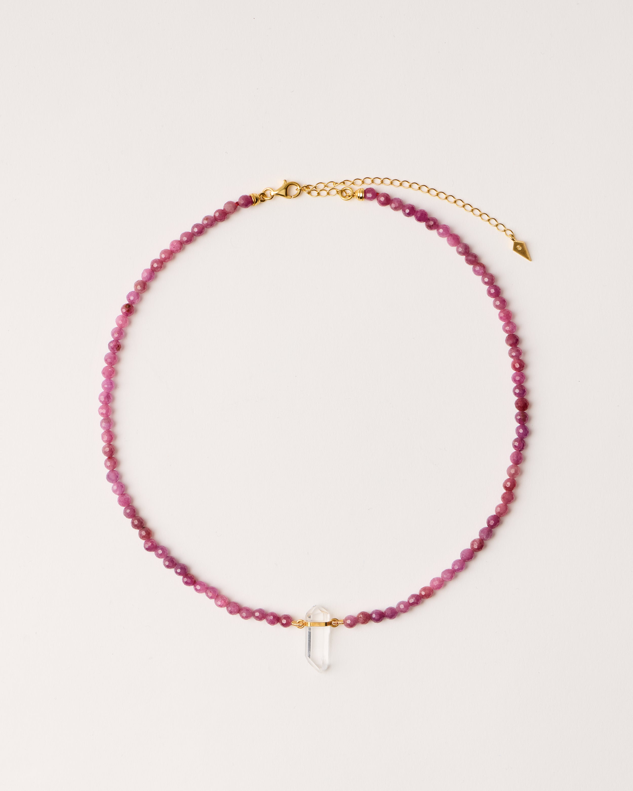 ENCARA CARMES Ruby necklace with raw polished quartz point pendant, gold-plated silver 8 cm extension chain and clasp, arrowhead-shaped fantasy signature, and 4 mm faceted ruby bead strand.