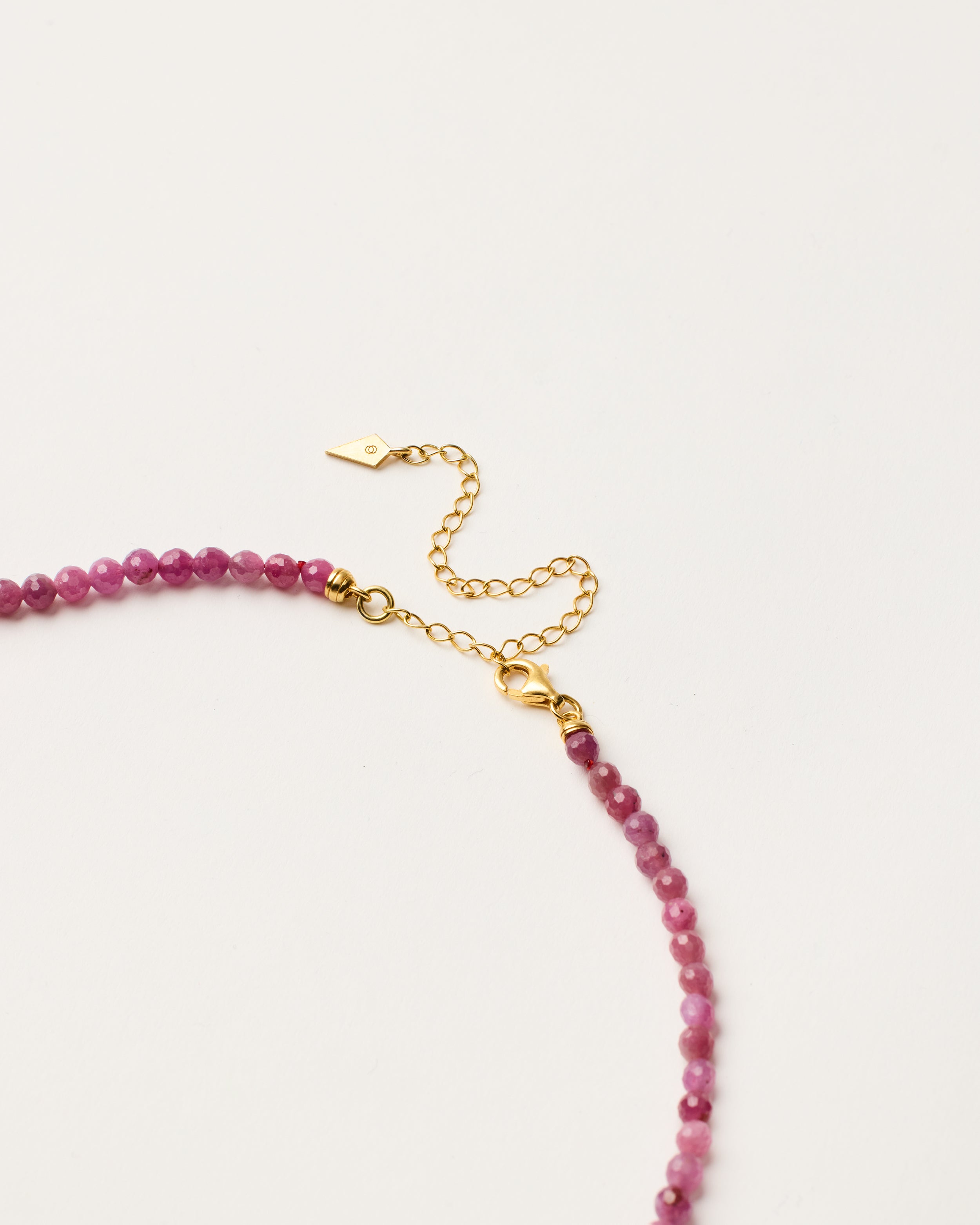 ENCARA CARMES Ruby necklace with raw polished quartz point pendant, gold-plated silver 8 cm extension chain and clasp, arrowhead-shaped fantasy signature, and 4 mm faceted ruby bead strand.