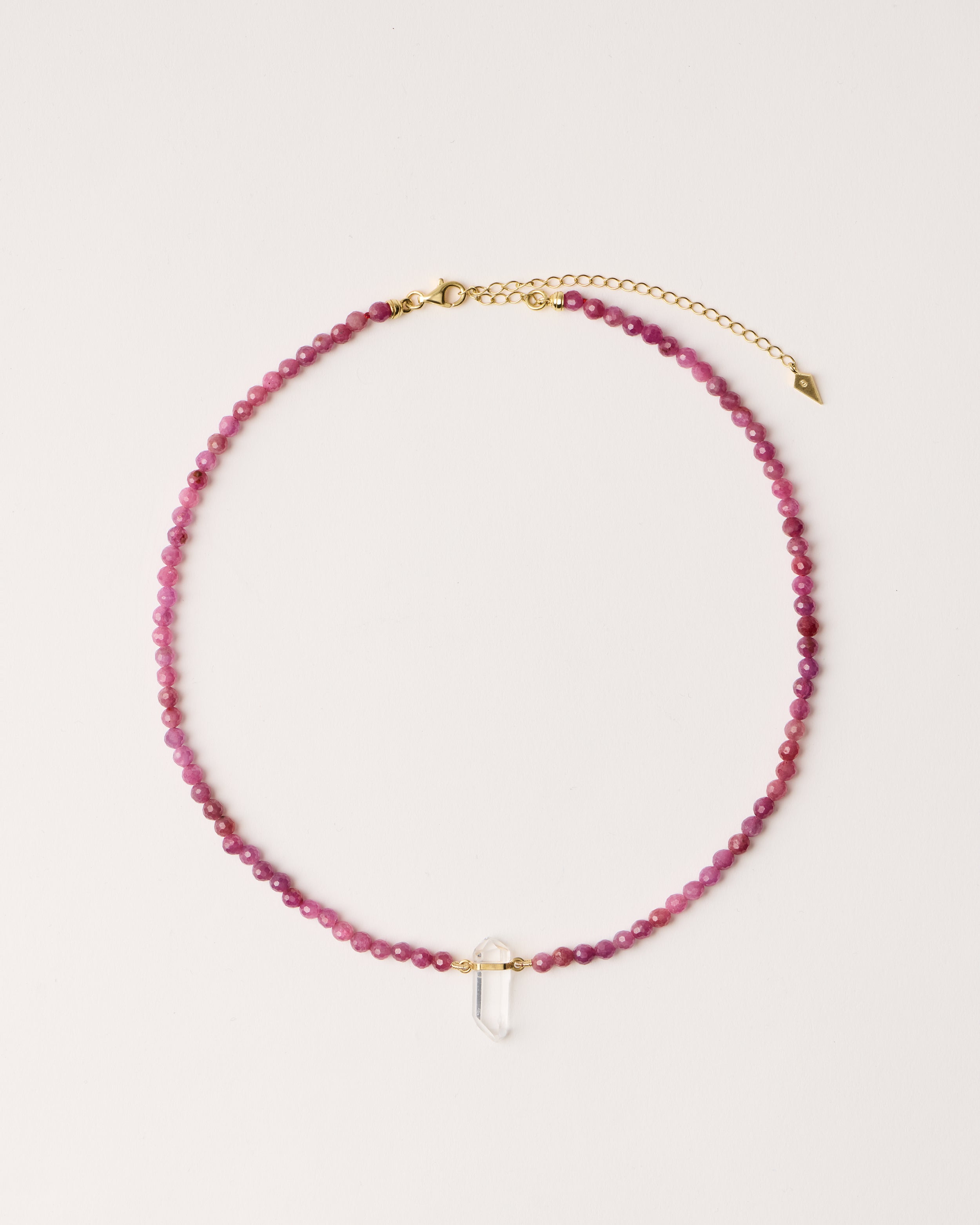 ENCARA CARMES Ruby necklace with raw polished quartz point pendant, gold 8 cm extension chain and clasp, arrowhead-shaped fantasy signature, and 4 mm faceted ruby bead strand.