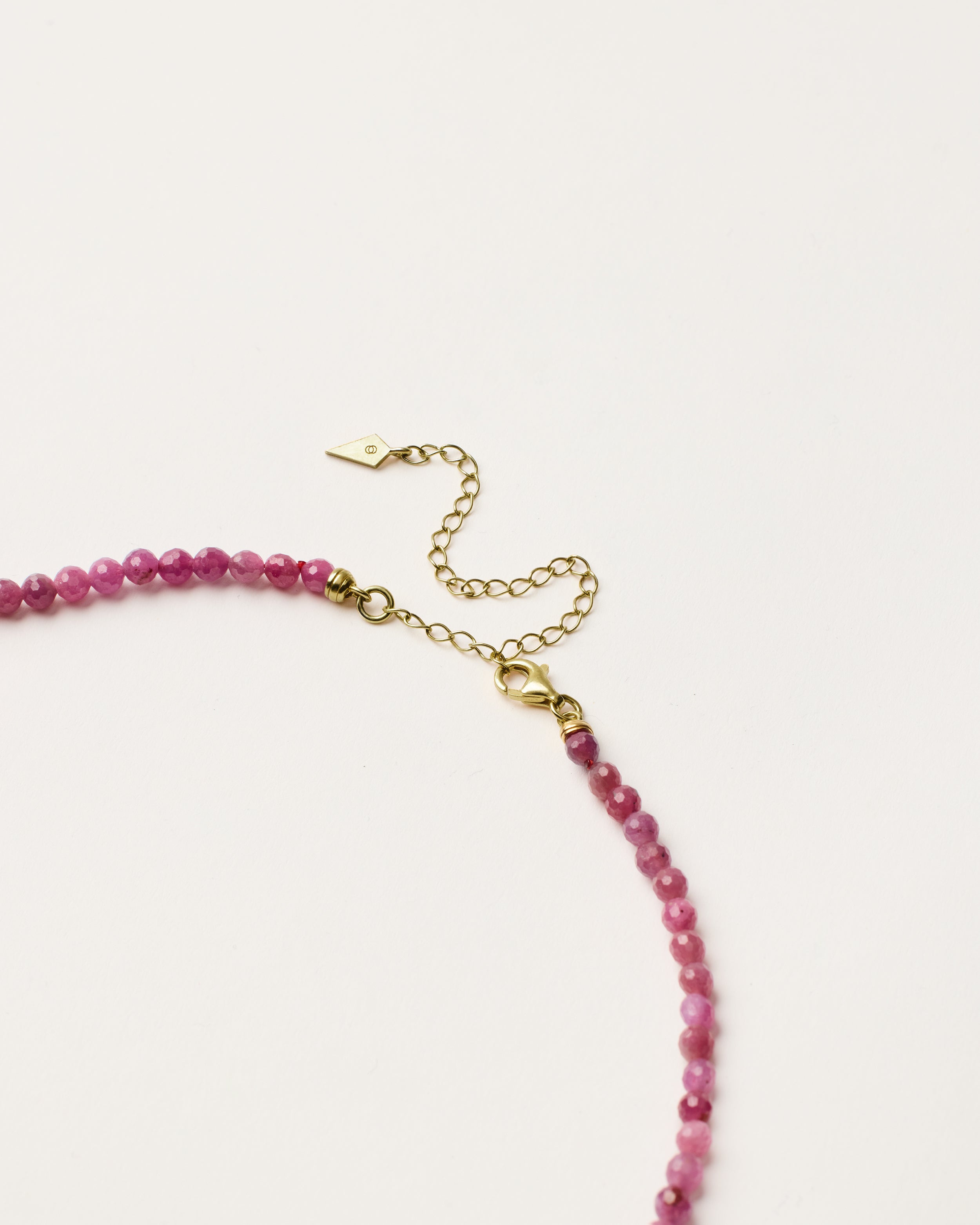ENCARA CARMES Ruby necklace with raw polished quartz point pendant, gold 8 cm extension chain and clasp, arrowhead-shaped fantasy signature, and 4 mm faceted ruby bead strand.