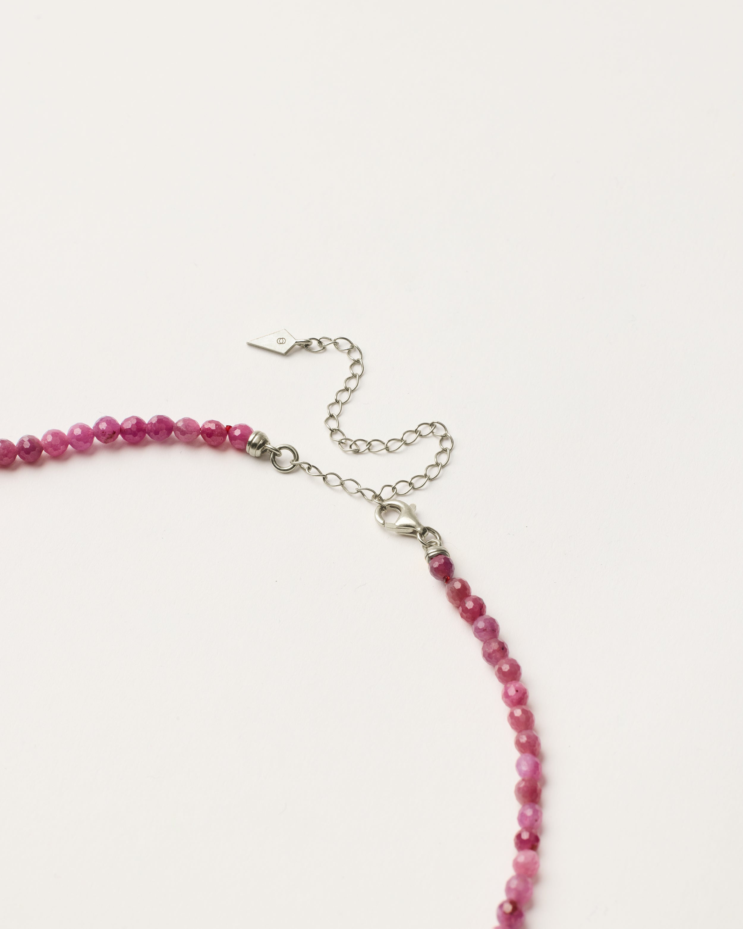 ENCARA CARMES Ruby necklace with raw polished quartz point pendant, silver 8 cm extension chain and clasp, arrowhead-shaped fantasy signature, and 4 mm faceted ruby bead strand.