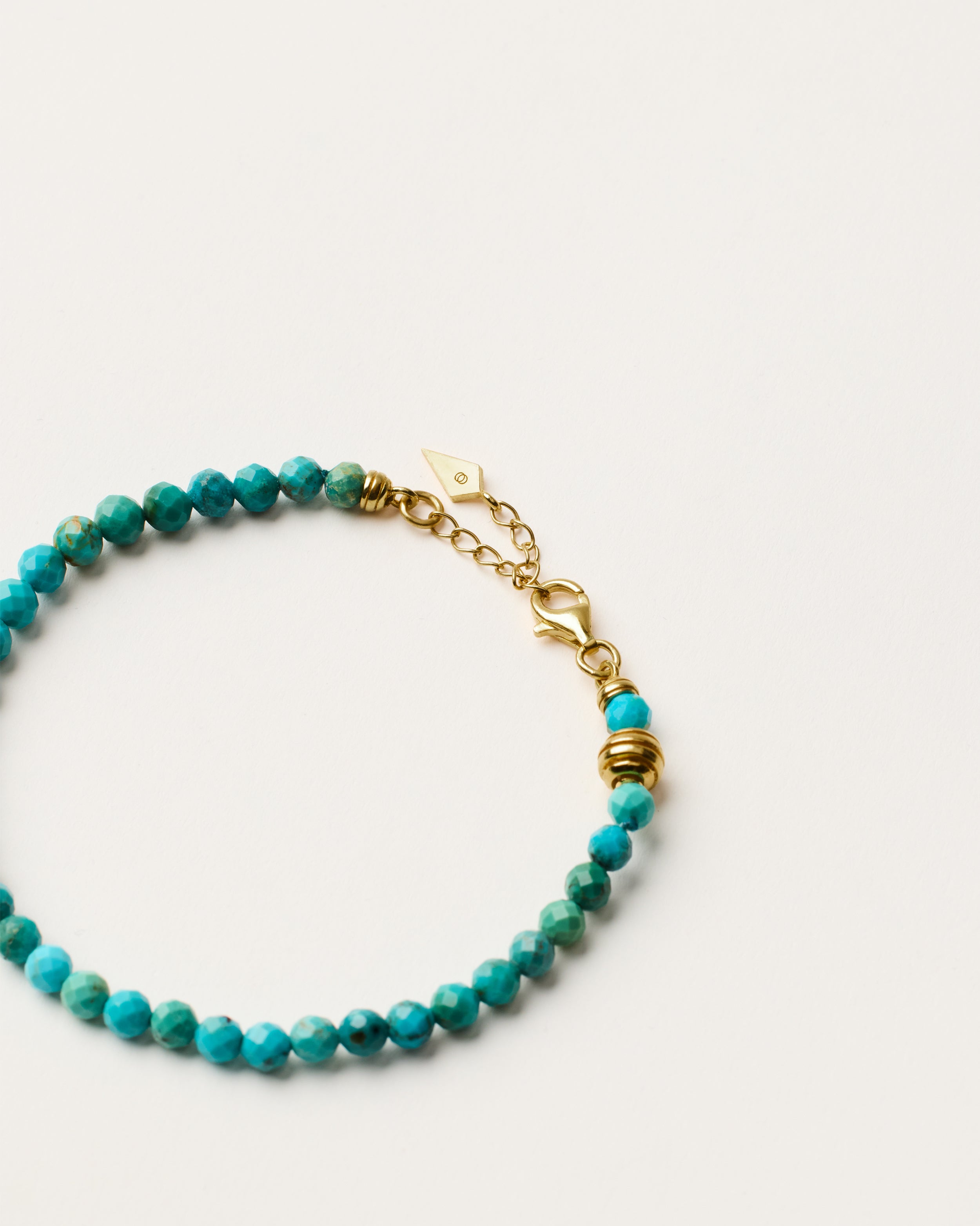 ETERNA AZURA Turquoise bracelet with polished gold spiral bead, 4 cm extension chain and clasp, arrowhead-shaped fantasy signature, and 4 mm faceted turquoise bead strand.