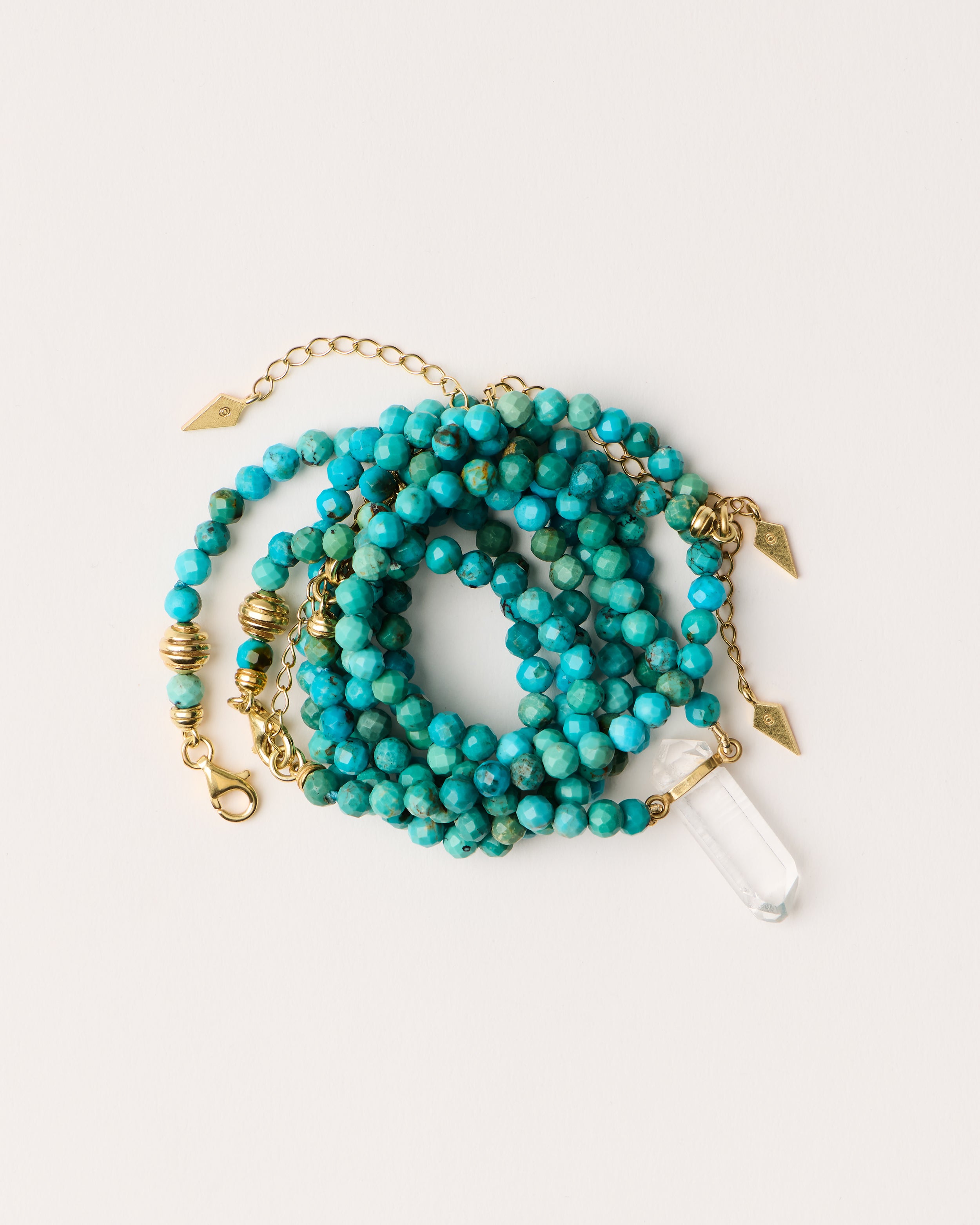 ENCARA / ETERNA AZURA Turquoise necklaces and bracelet with polished gold spiral bead, extension chain and clasp, arrowhead-shaped fantasy signature, and 4 mm faceted turquoise bead strand and raw polished quartz point pendant.